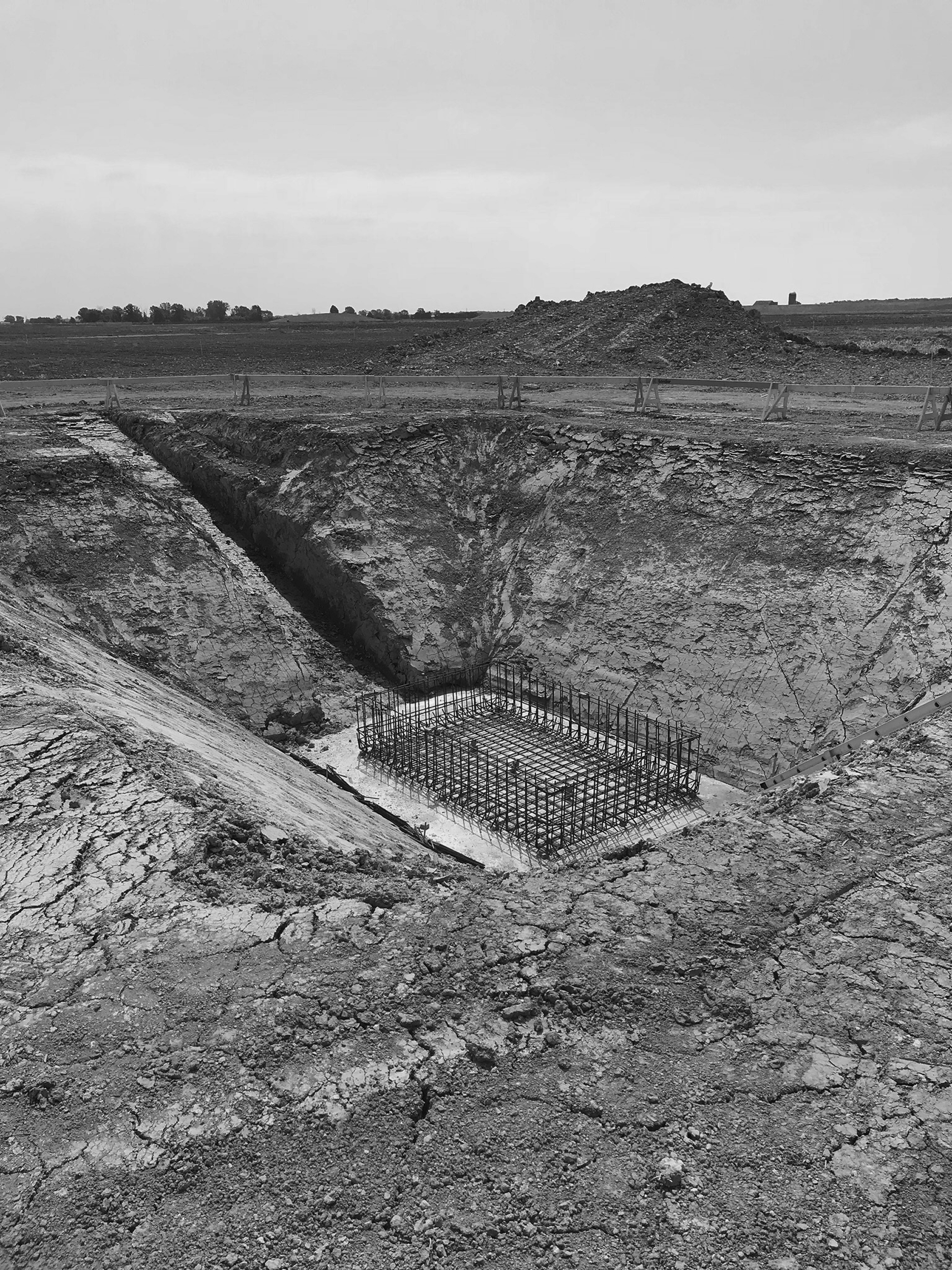 Construction site with exposed ground and steel rebar foundation in a rural landscape