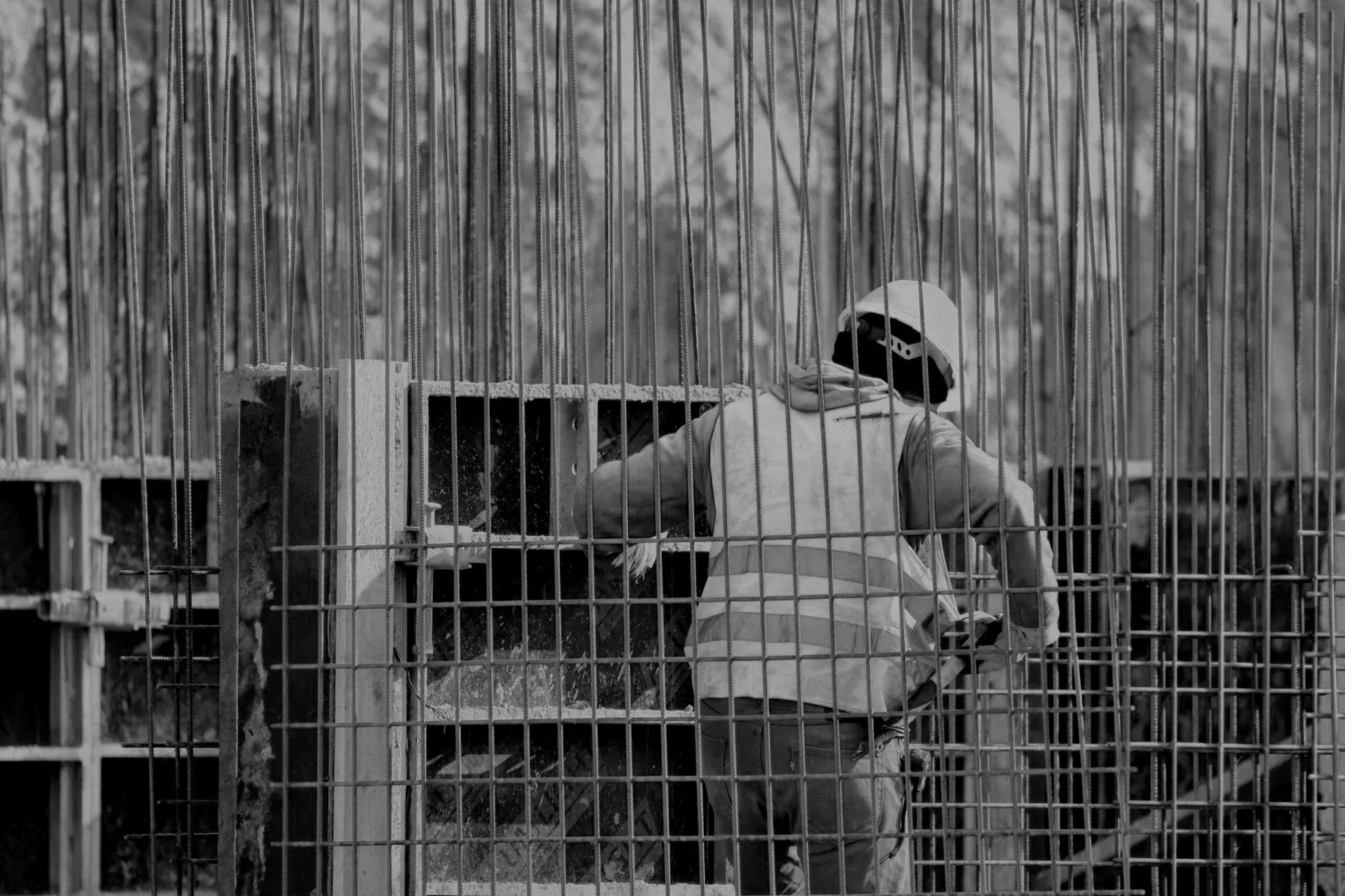 A person wearing a helmet and jacket working on a construction site behind a metal fence.