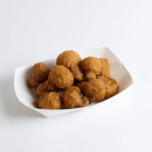 Several fried chicken nuggets in a white paper serving boat on a white surface.