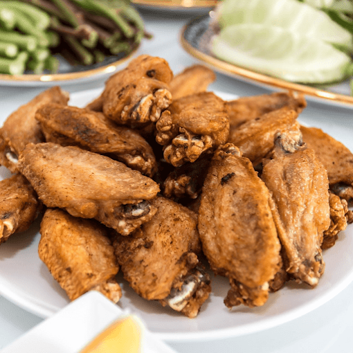 Plate of fried chicken wings with two side dishes, one containing green beans and the other containing cabbage.