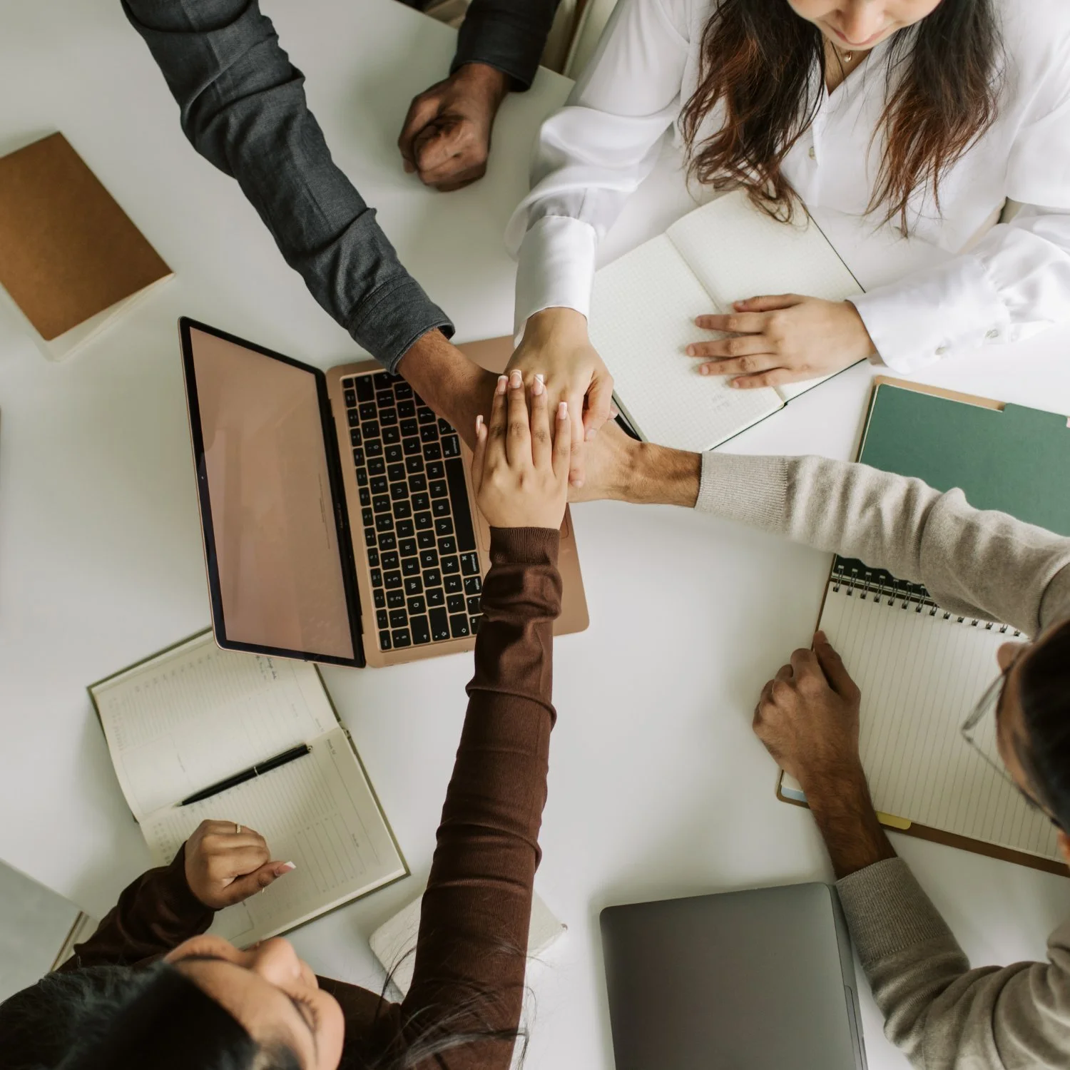 Team joining hands over a desk, representing a strong, unified hire