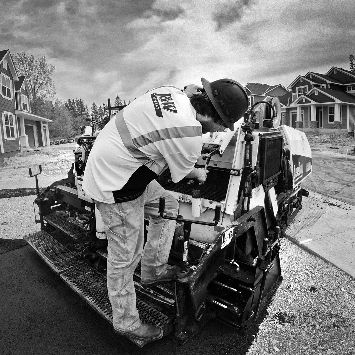 J&W Asphalt crew member operating an asphalt paver on a new residential street lined with newly built homes