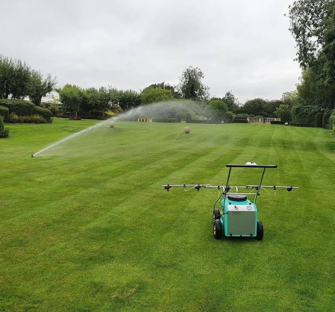 A lawn sprinkler in operation watering a green grassy field, with a portable hose reel sprinkler in the foreground on a cloudy day.