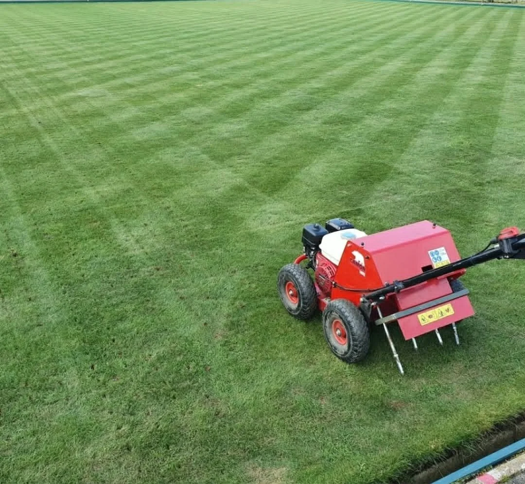 A red lawn mower on a green, freshly mowed soccer field.