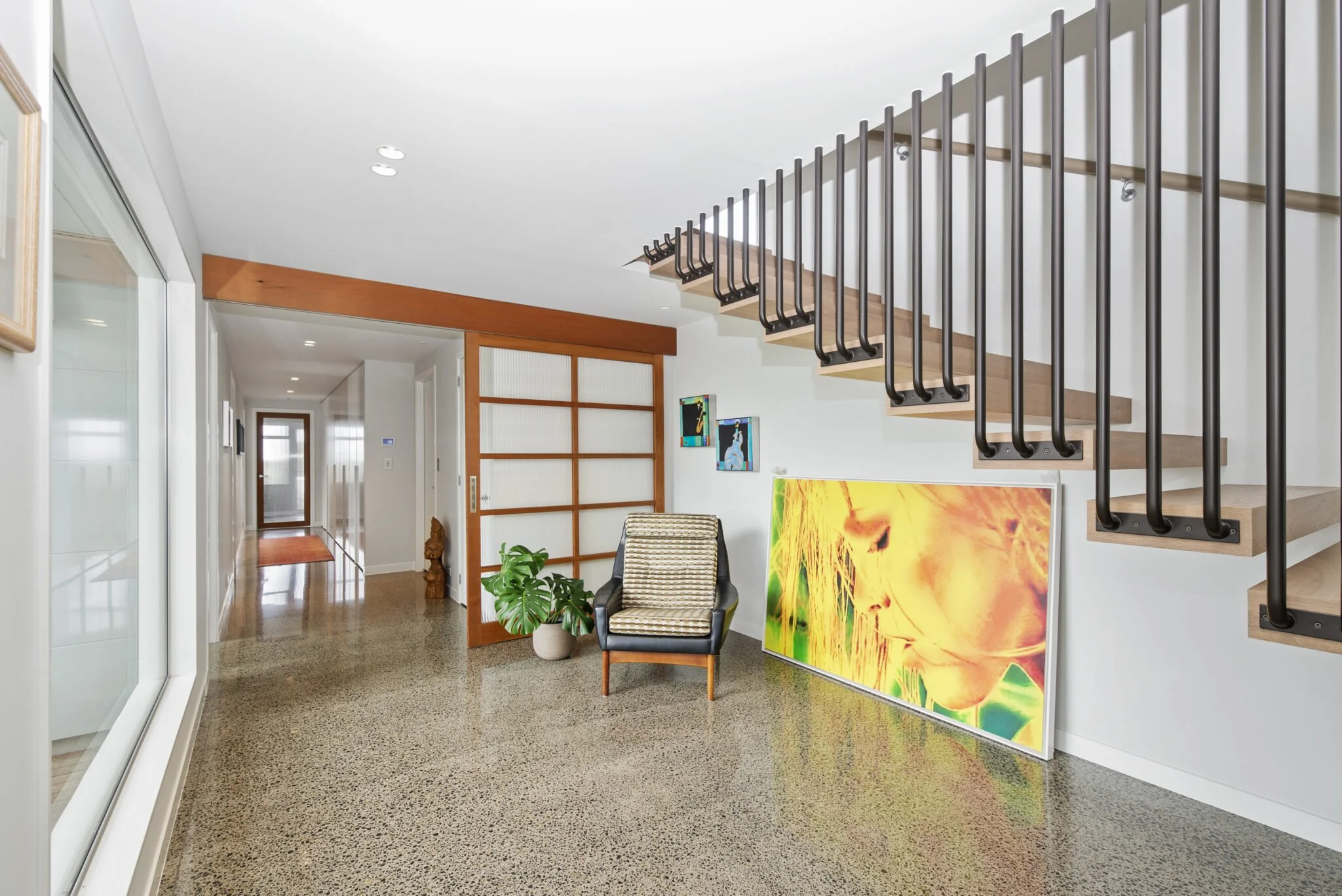 Interior of a modern house with a staircase, colorful paintings, a chair, and a decorative plant.