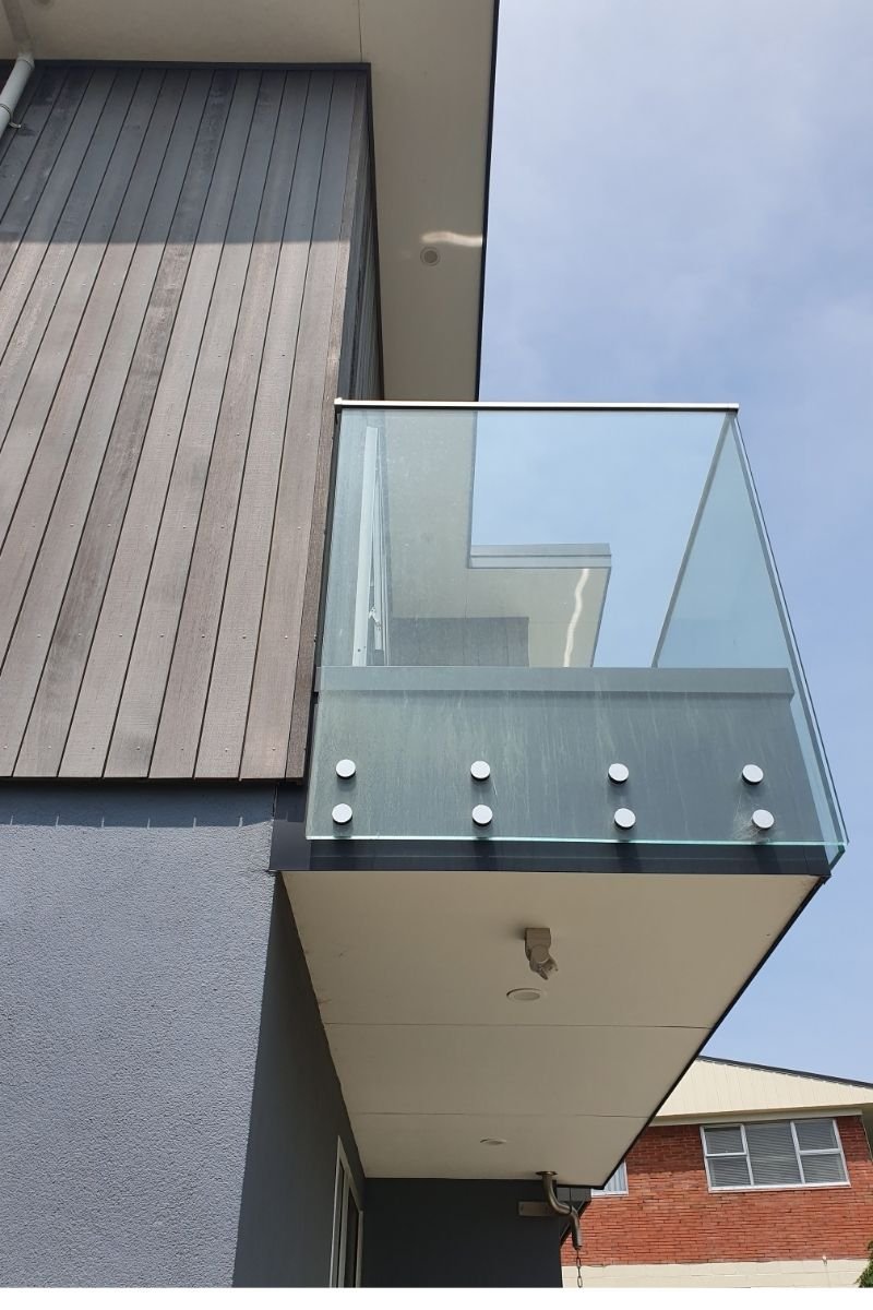 Modern building with a glass balcony and wooden exterior paneling, under a clear blue sky