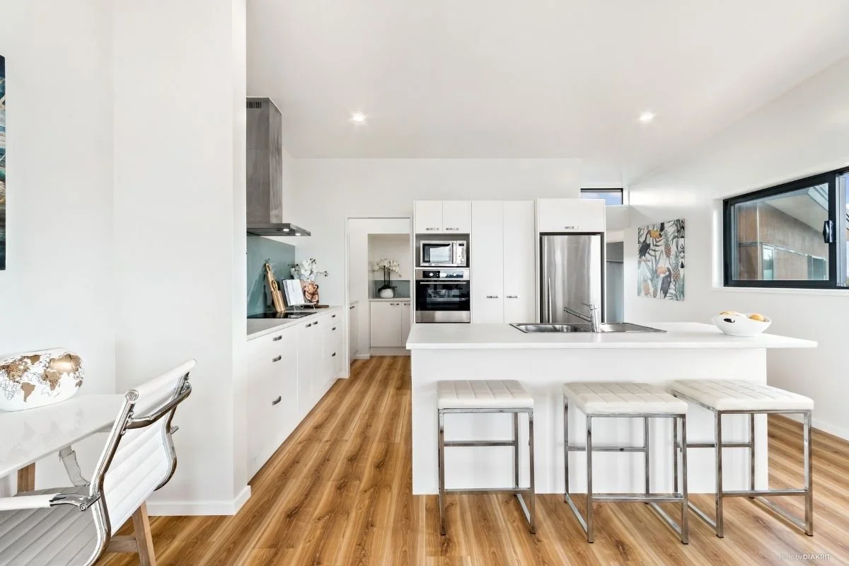 Modern white kitchen with wood floor, stainless steel appliances, and an island with seating for three
