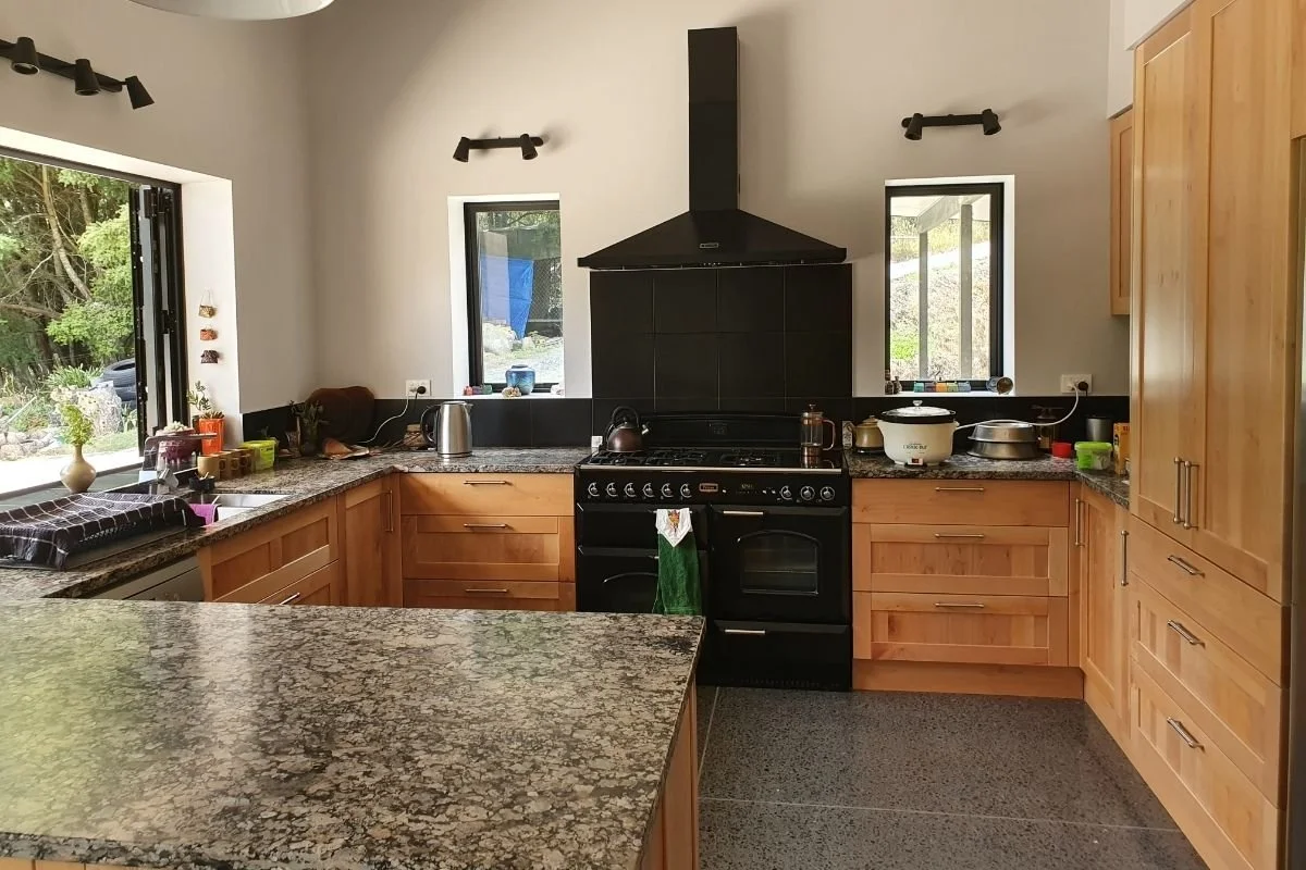 Kitchen with granite countertops, wooden cabinets, black stove with black range hood, two windows, and various kitchen items on the counter.