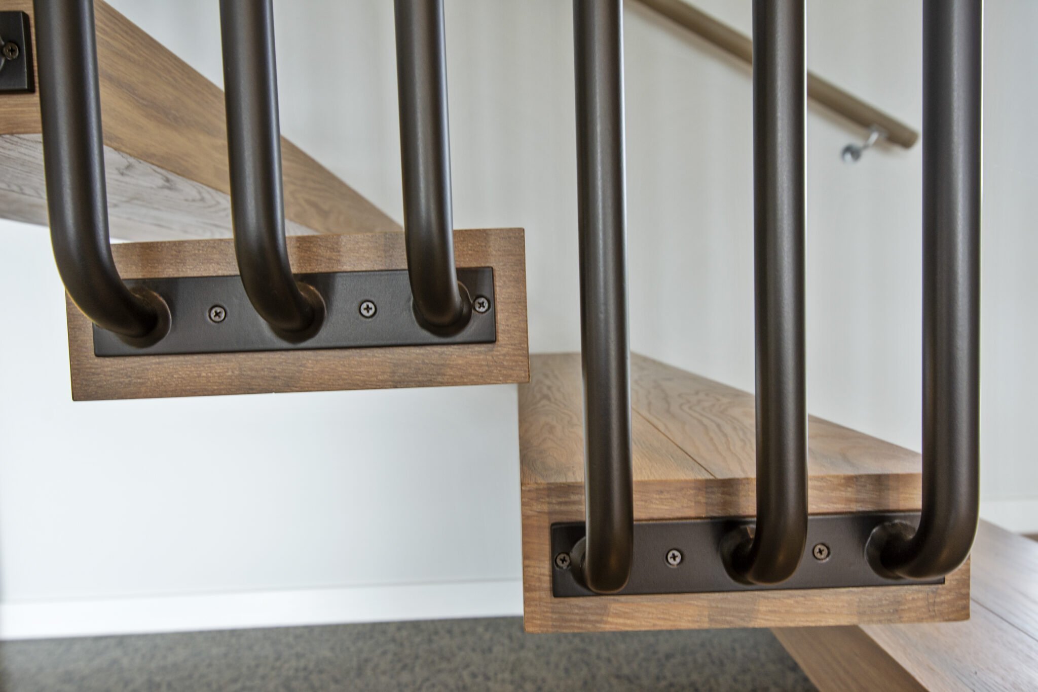 Close-up view of a staircase railing with black metal bars and wooden handrails in a modern interior setting.