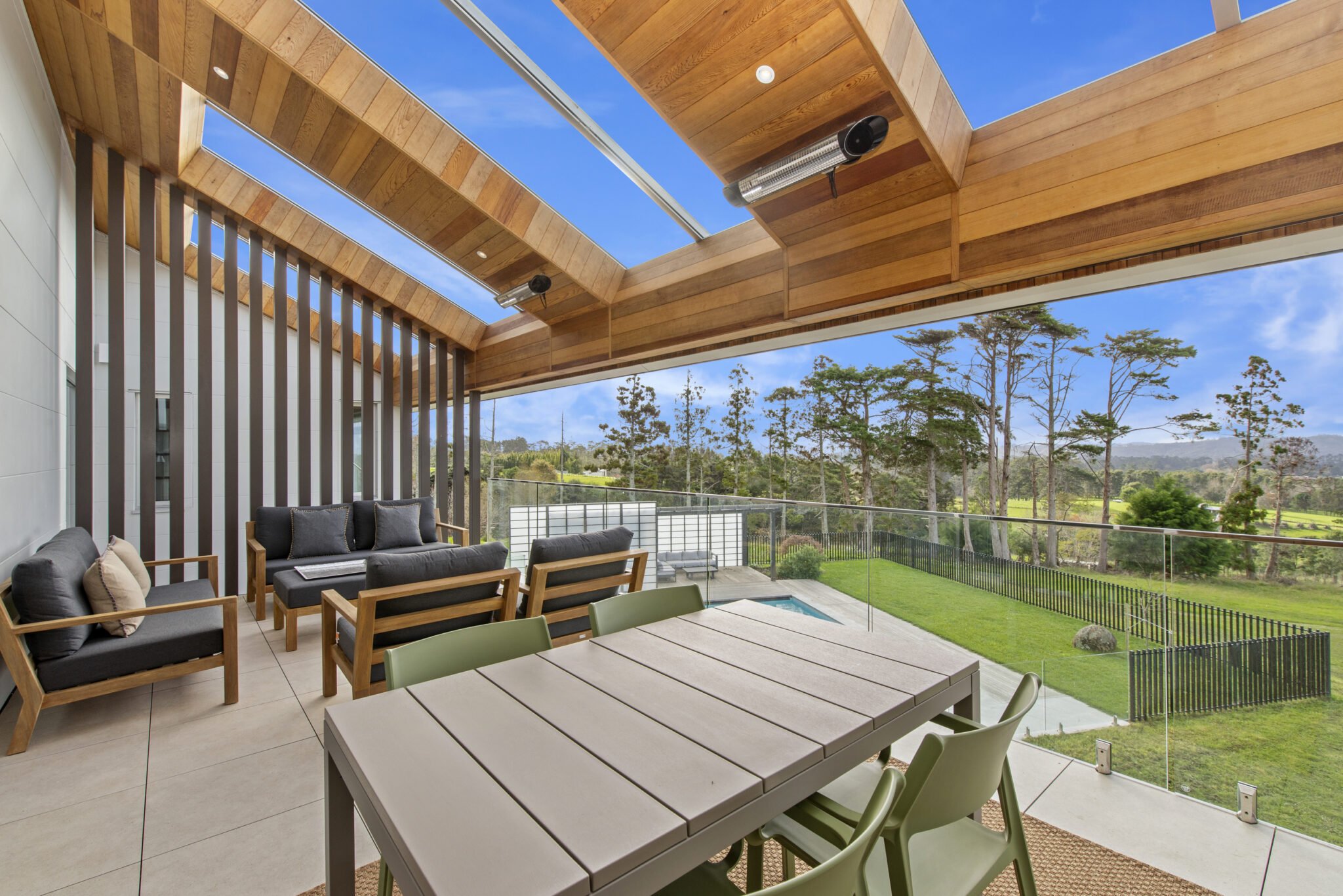 A covered outdoor patio with seating and dining areas overlooking a lush green landscape with trees and blue sky.