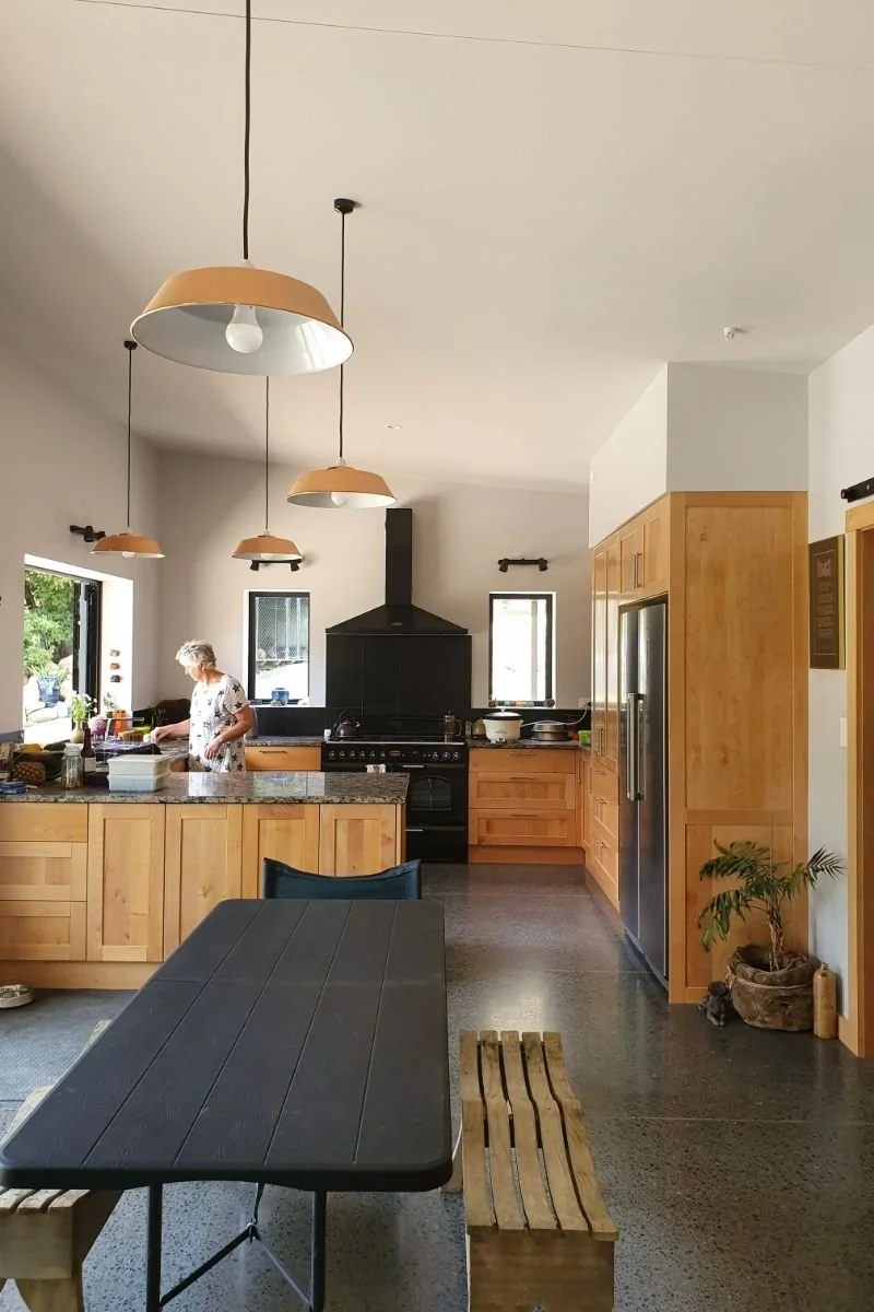 A woman preparing food in a kitchen with wooden cabinets, a black stove, and pendant lights hanging from the ceiling.