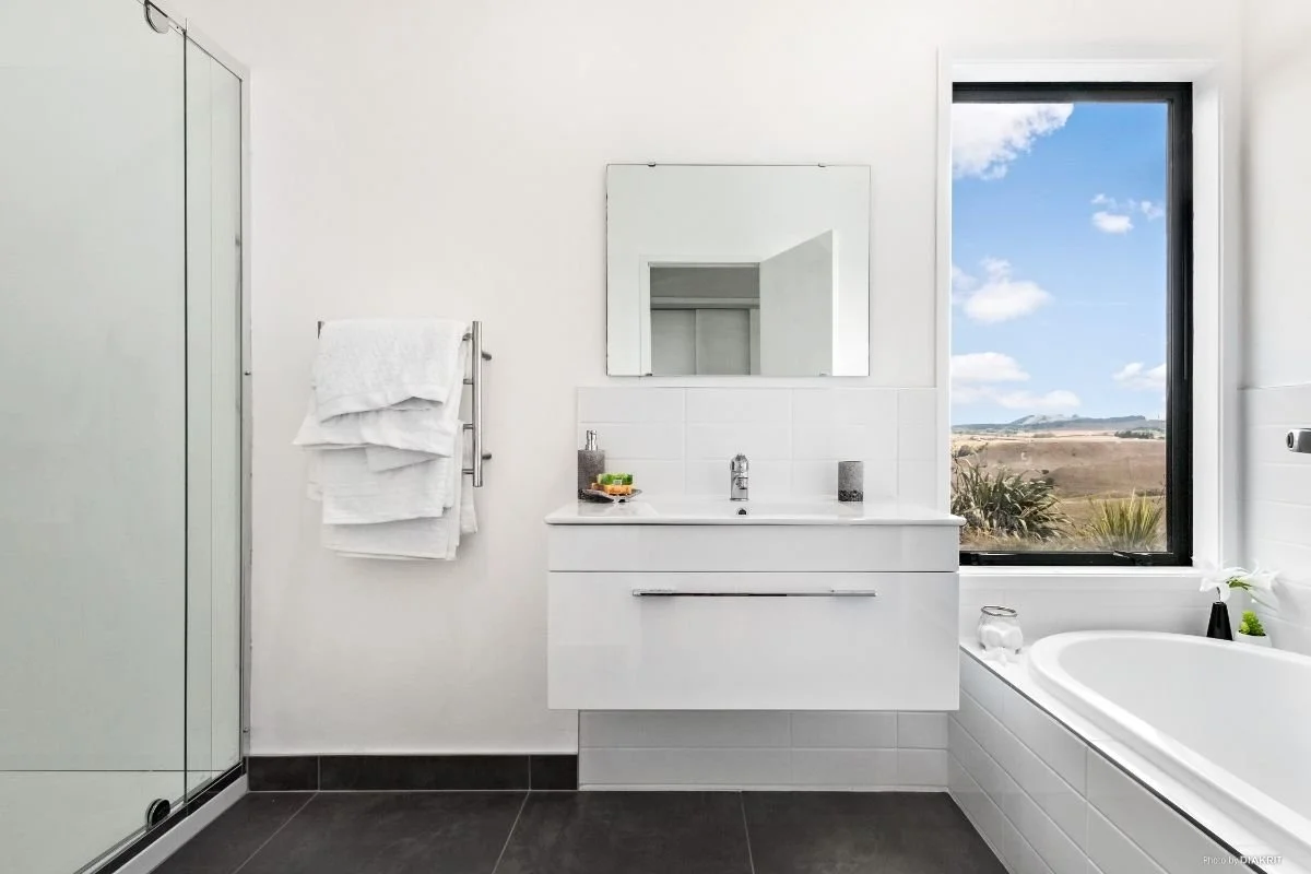 Modern bathroom with white walls and sink, mirror, window showing outdoor landscape, and bathtub