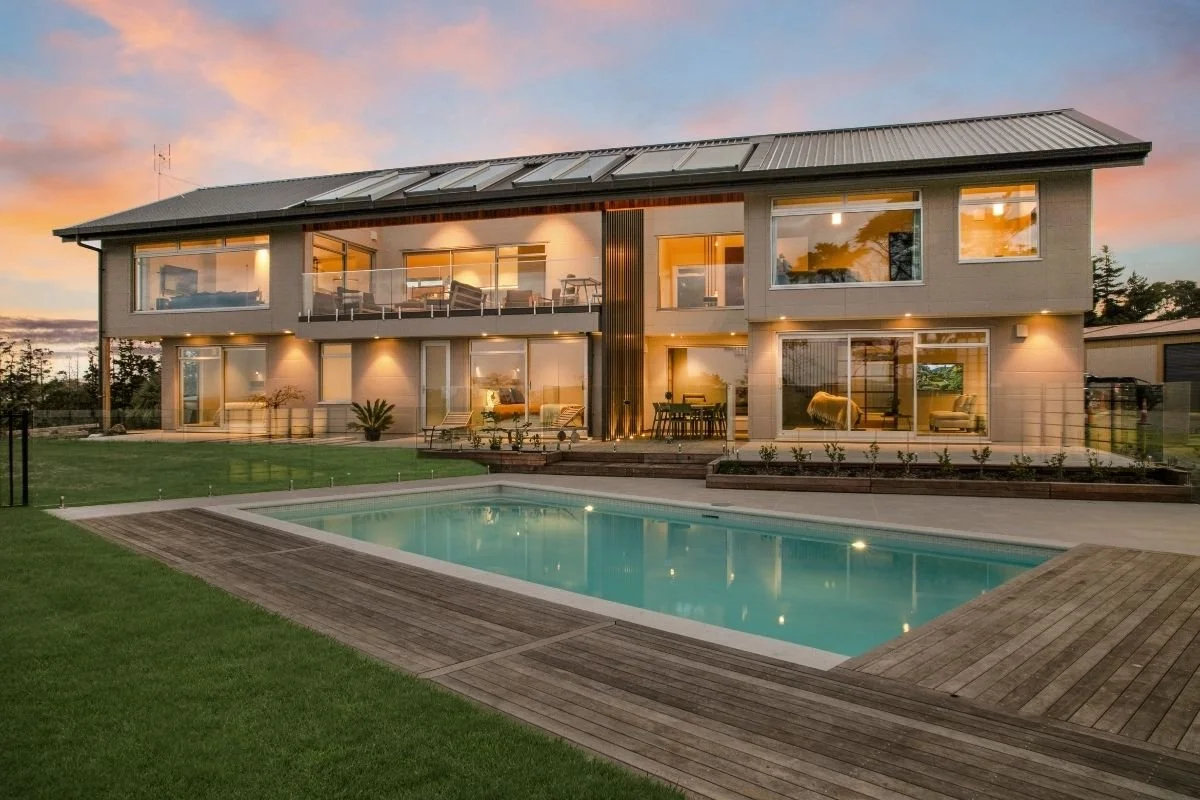 Modern two-story house with large glass windows and a backyard swimming pool at sunset.
