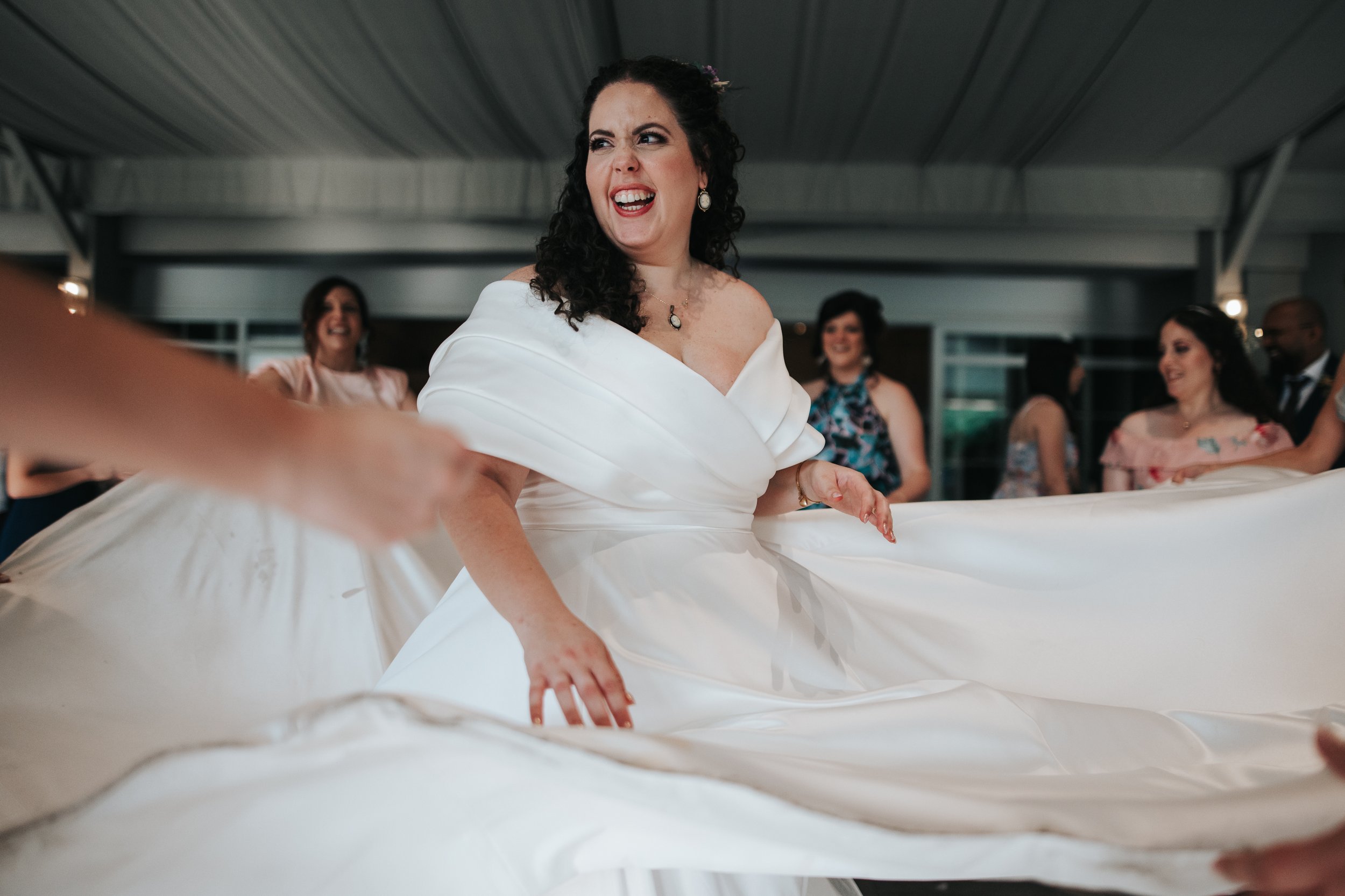A woman in a white dress smiling and dancing at a celebration with friends inside a modern building.