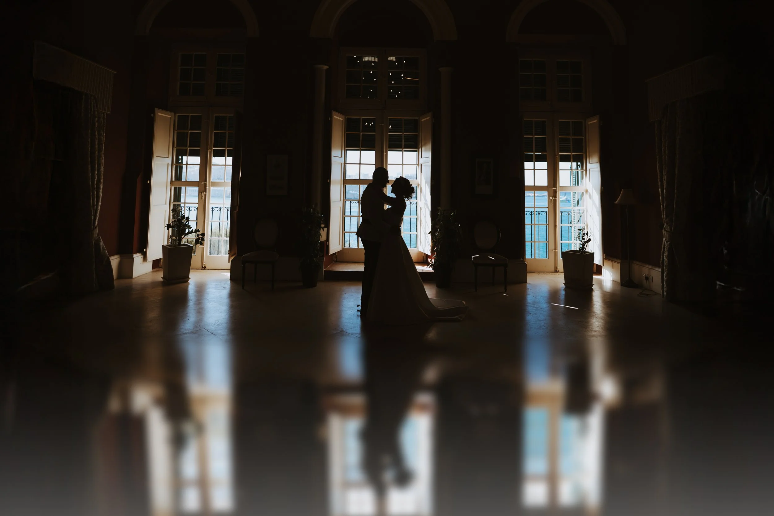 Silhouette of a couple dancing in front of large windows in a dimly lit room.
