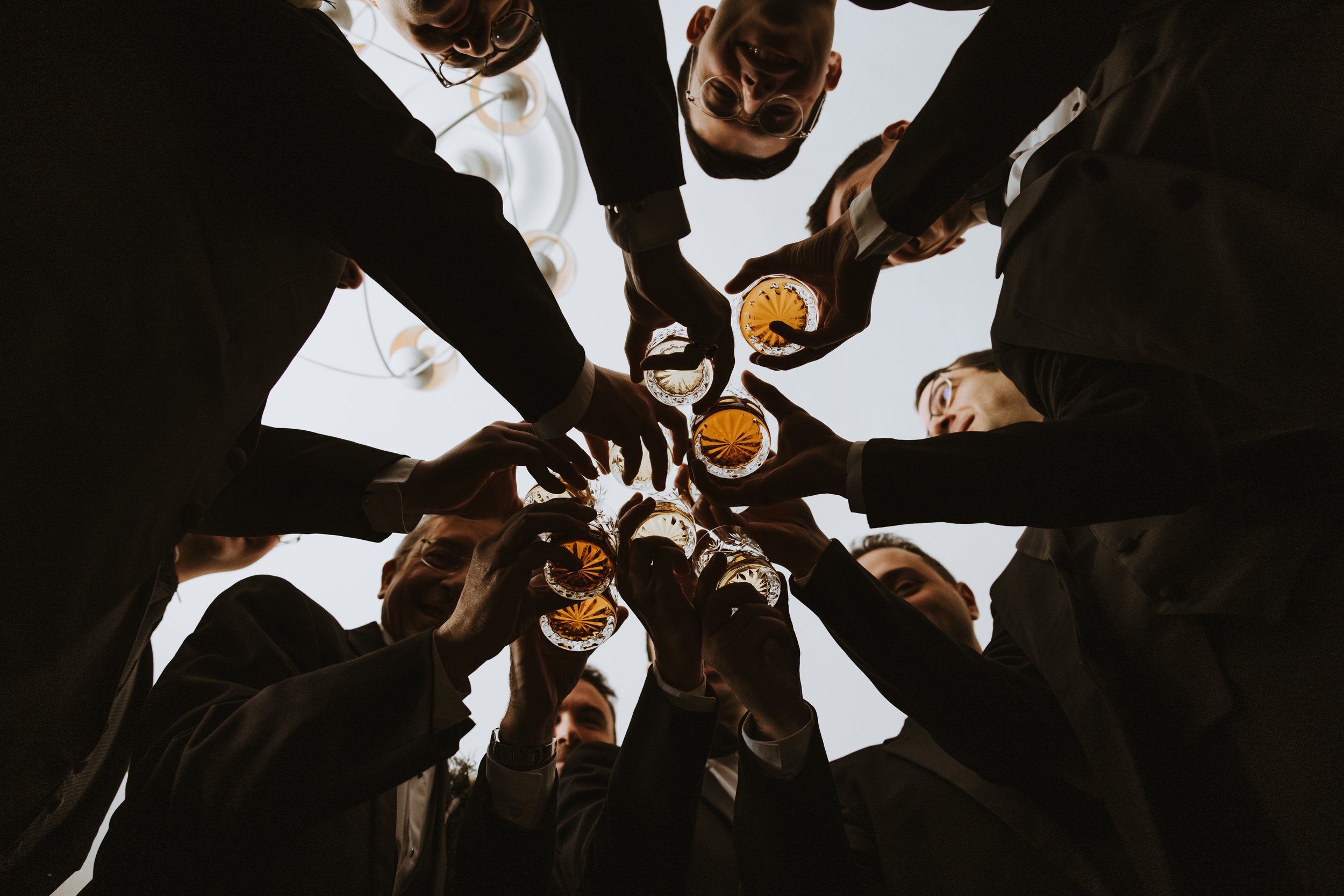 Group of people in formal attire celebrating with drinks, seen from below against a light background.