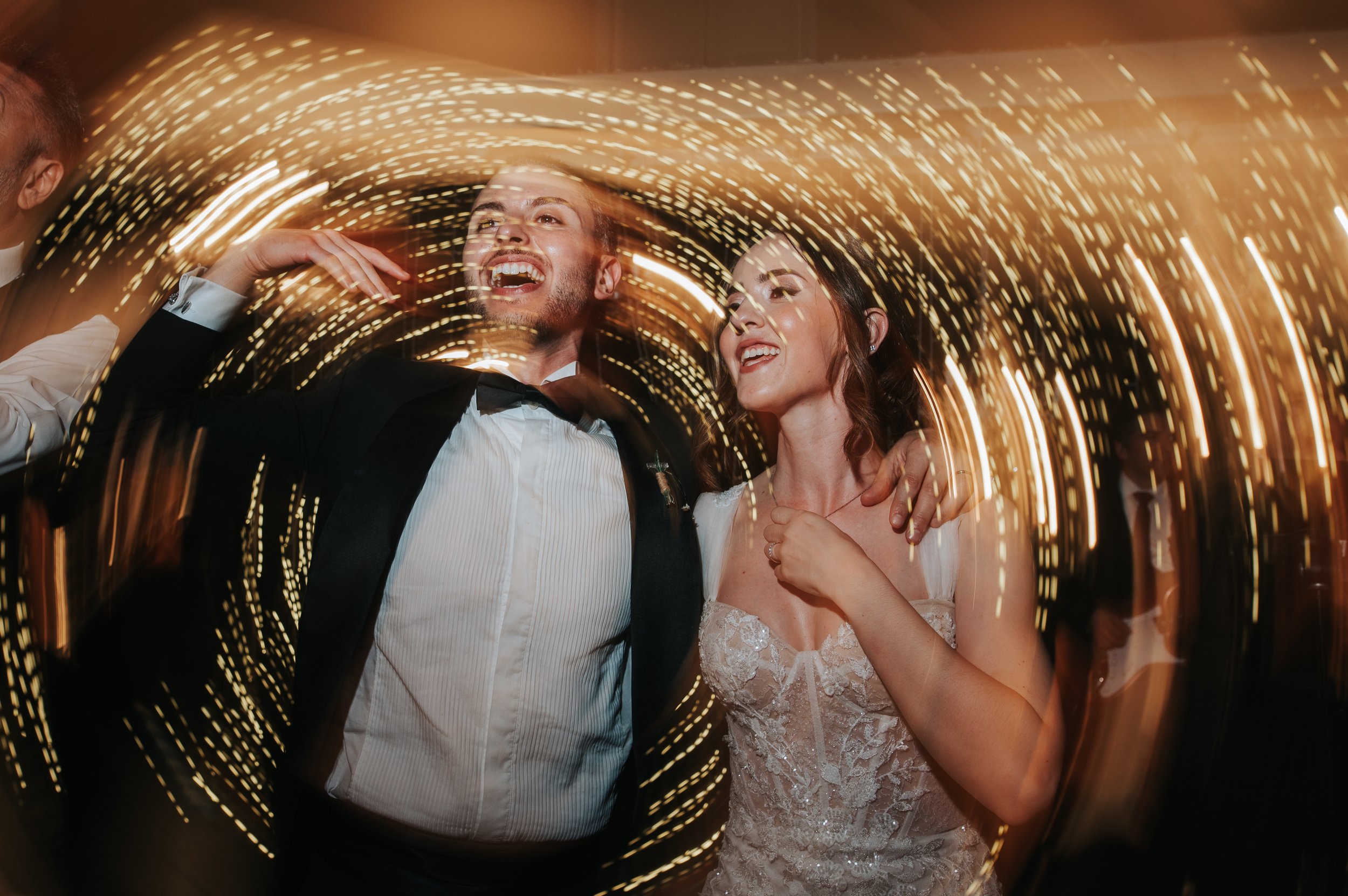 A newlywed couple dancing at their wedding reception with swirl lights around them.