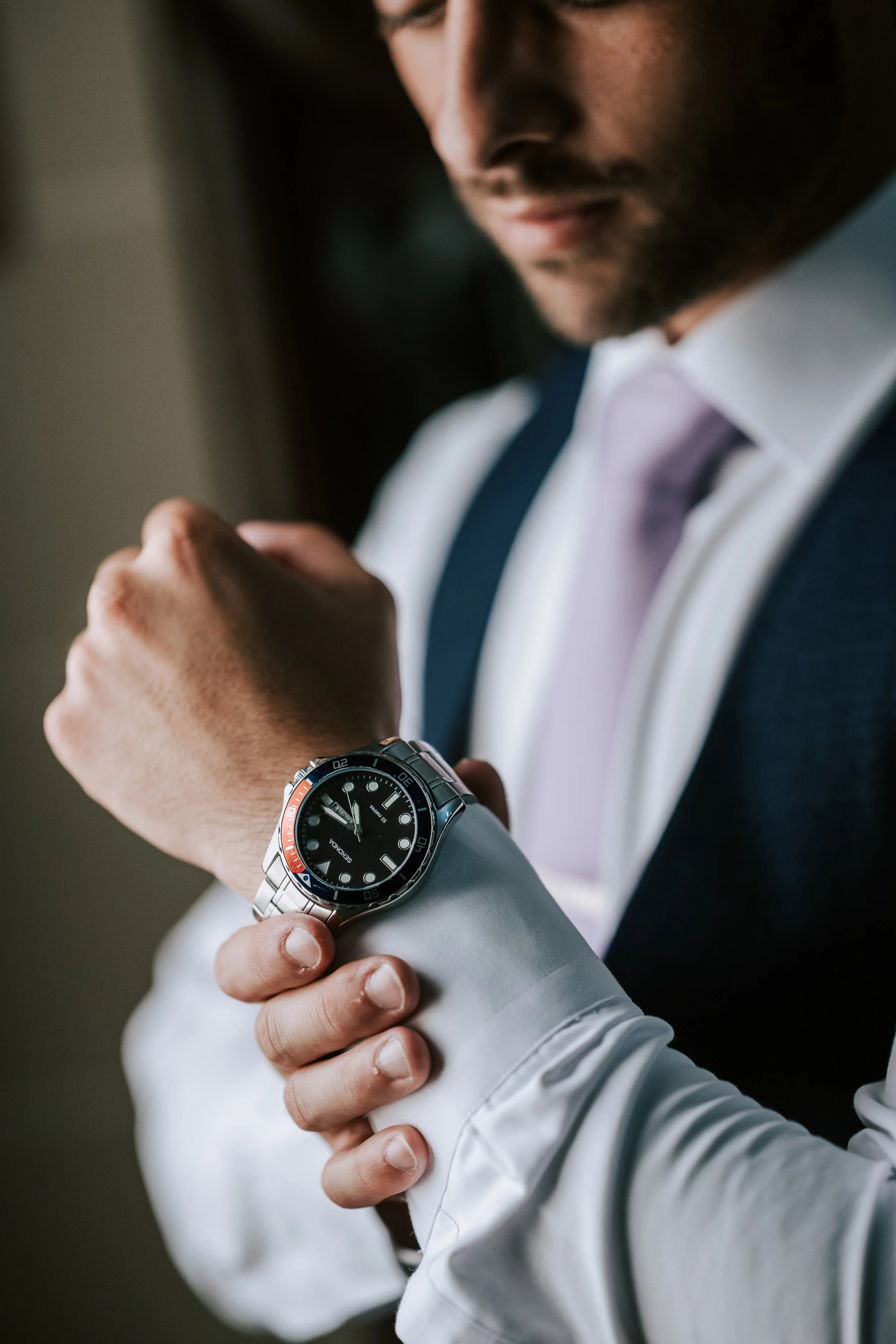 Man in a suit adjusting his watch on his wrist, wearing a white shirt and tie.