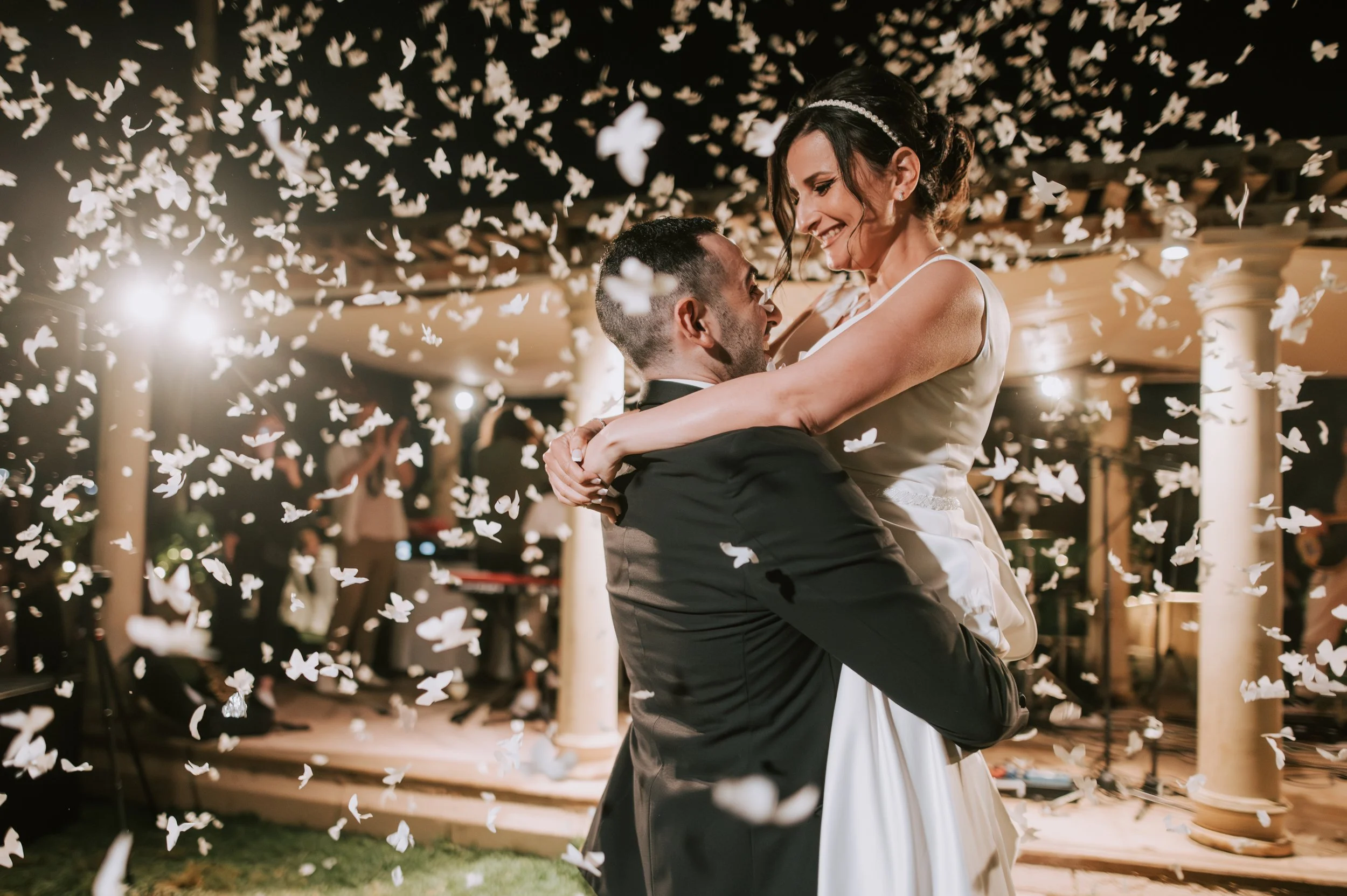 A bride and groom dancing at their wedding reception surrounded by falling white paper butterflies.