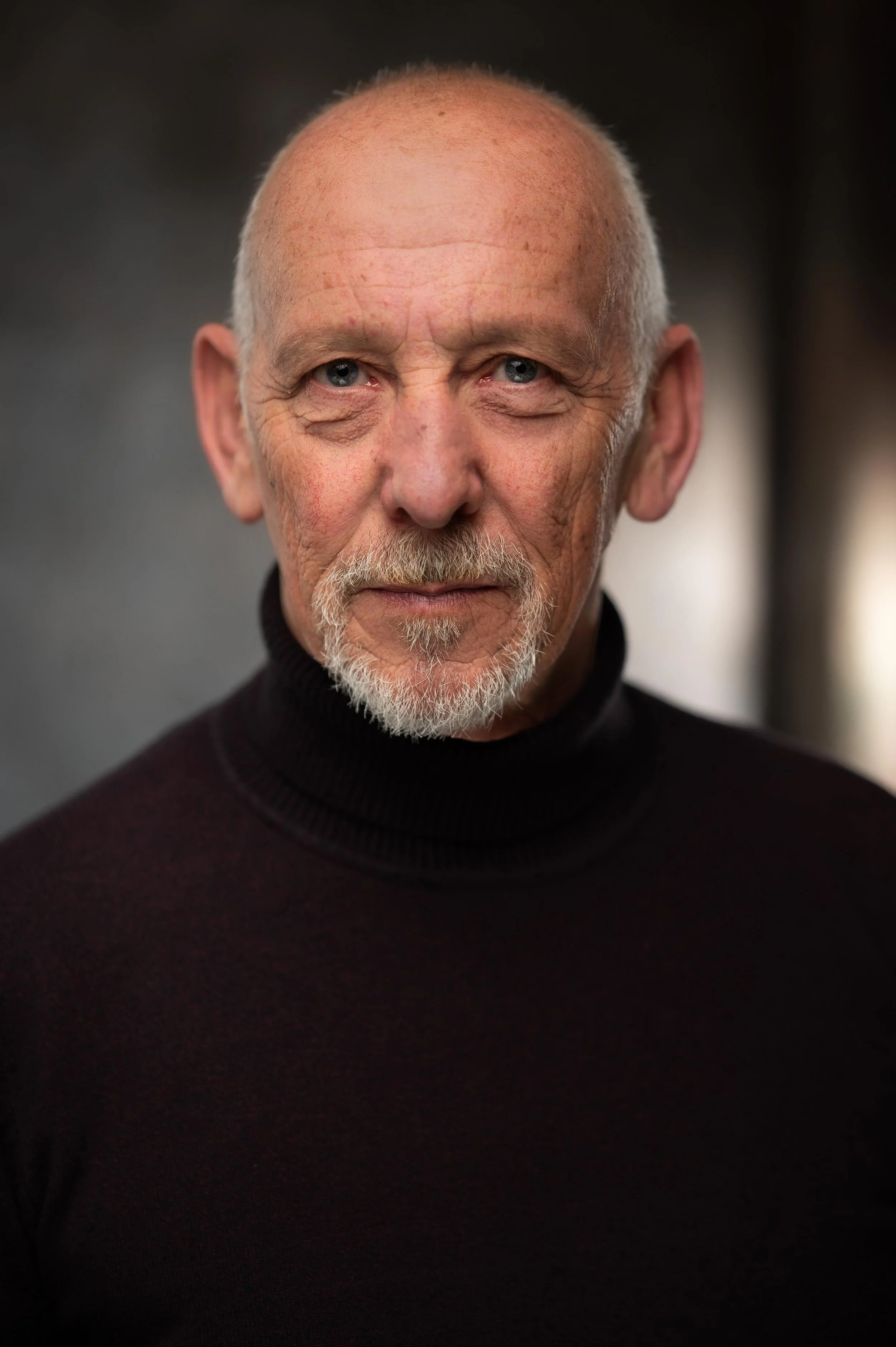 Close-up portrait of Stephen Oliver, blue eyes, and a white goatee, wearing a black turtleneck sweater.