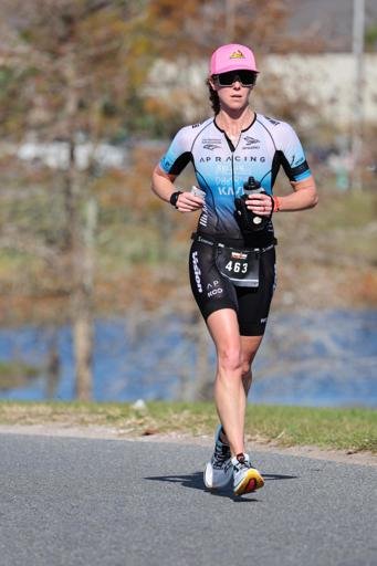 Female runner in a triathalon, Dr. Sara Black, pelvic floor physical therapist, wearing helmet, sunglasses, sports jersey, shorts, and running shoes.