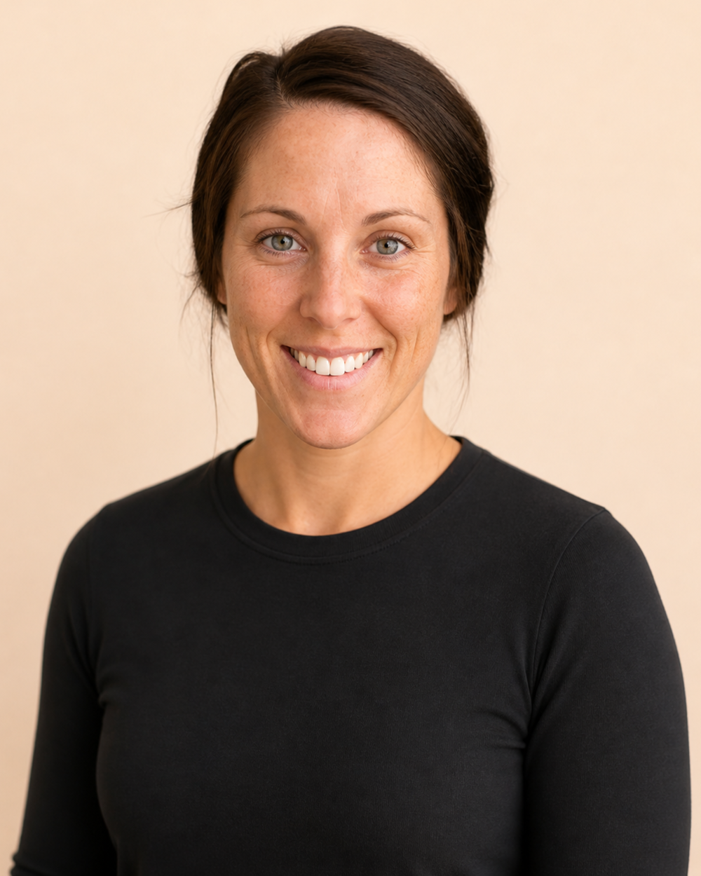A woman with short dark hair, wearing a black top, smiling against a plain beige background.