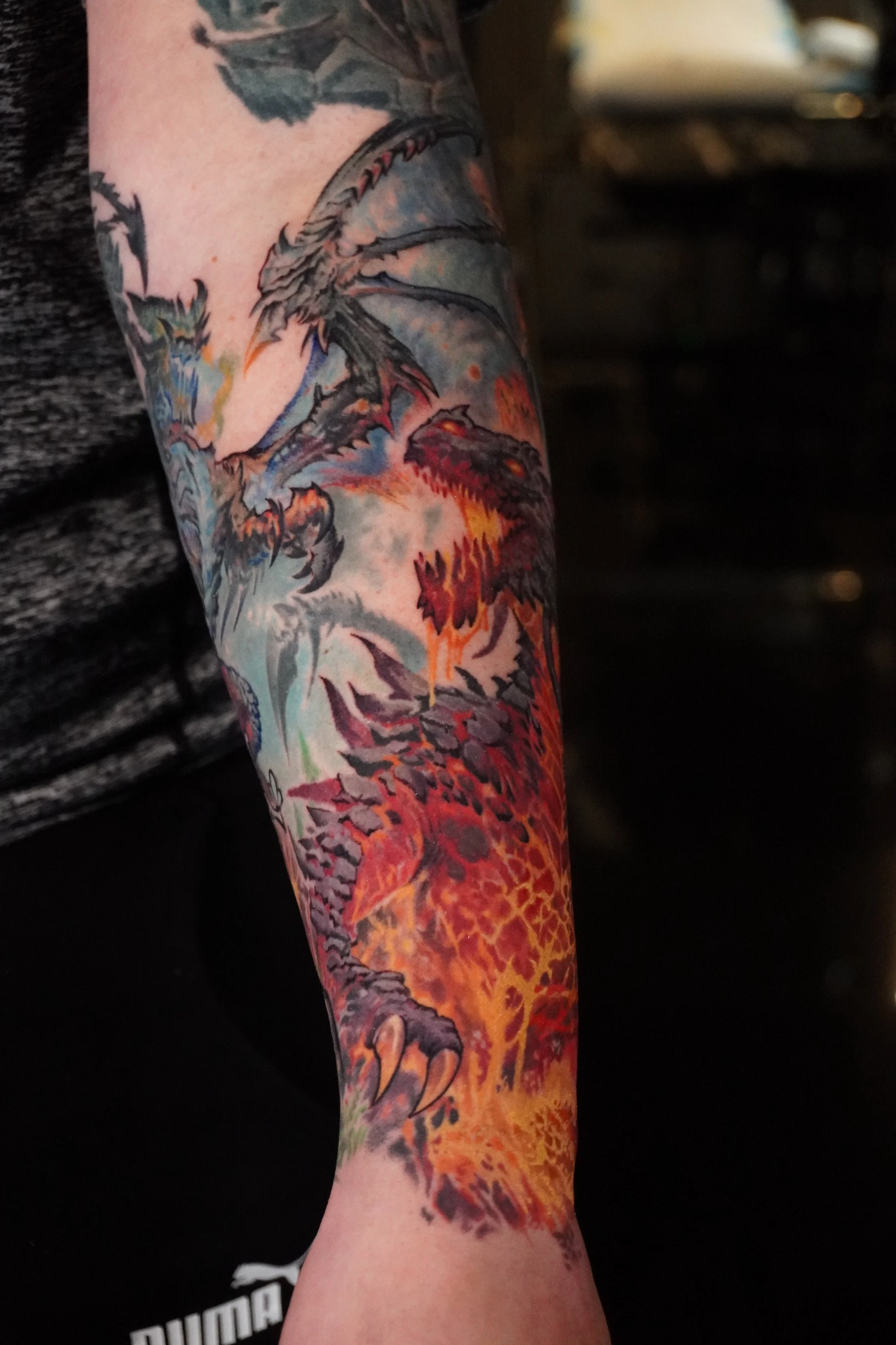 Colorful tattoo of a dragon on a person's arm, with fiery shades of red, orange, and yellow, set against a cloudy, stormy background.