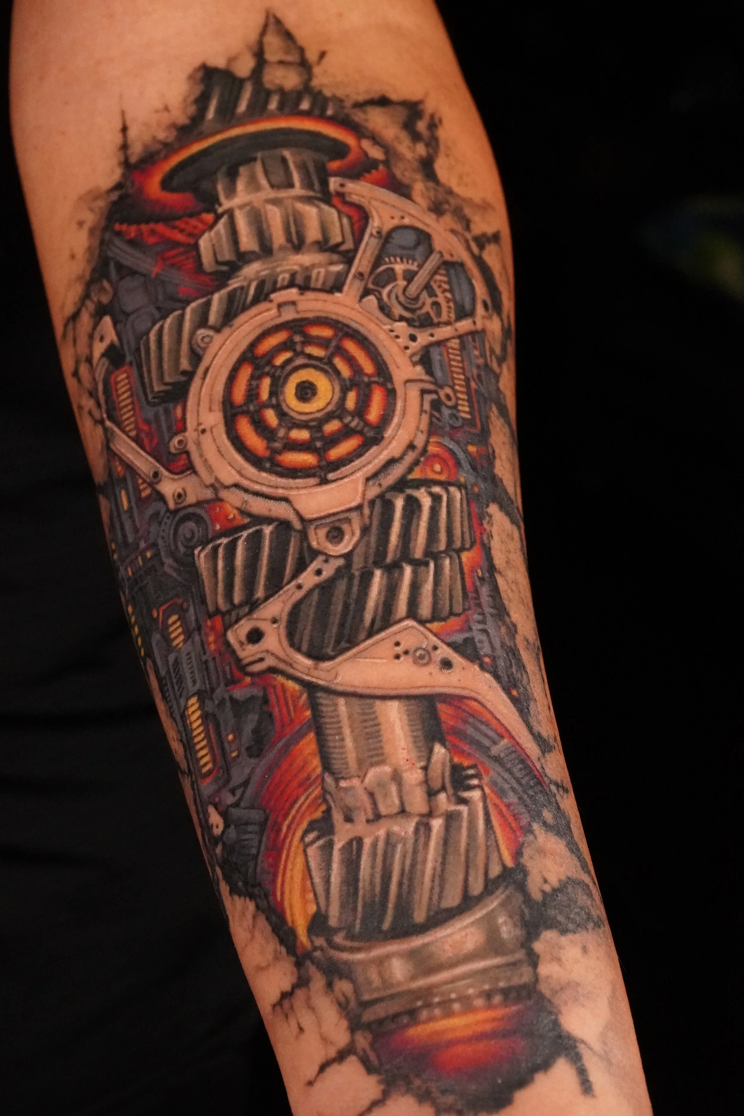 Tattoo of a mechanical gear system with fiery and smoky background on a person's arm.