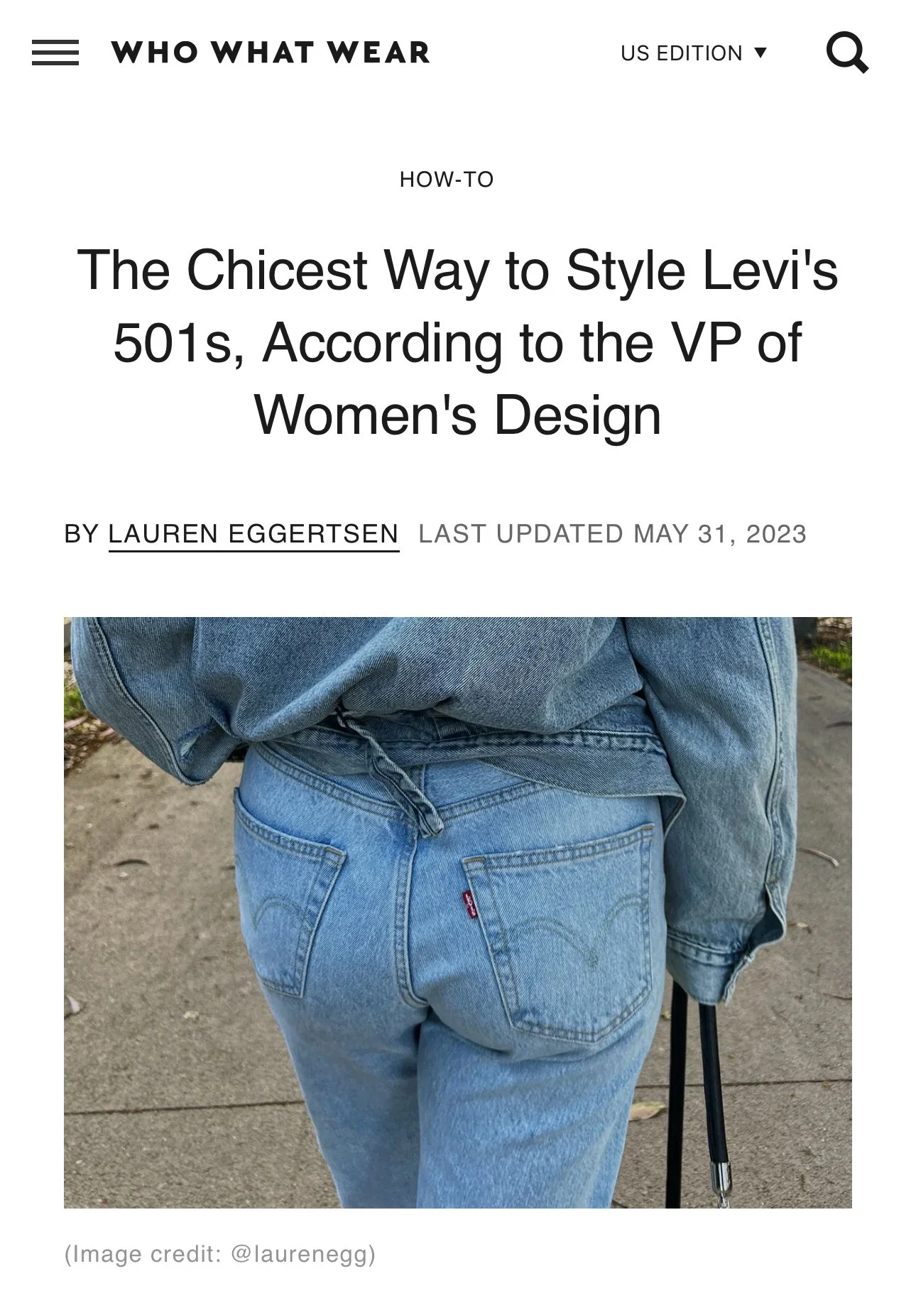 Close-up of a person wearing high-waisted light blue jeans and a dark gray oversized sweatshirt, walking outdoors with a walking cane.