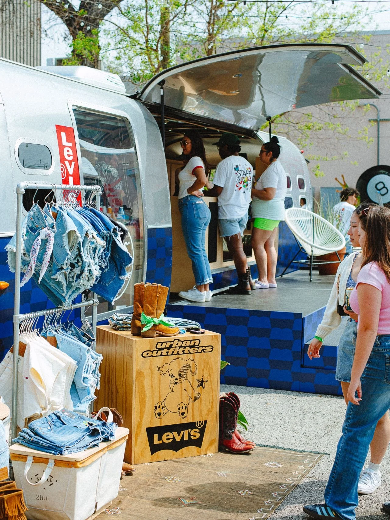 People shopping at a mobile retail store with Levi's clothing on display, outdoor setting with trees and other customers nearby.