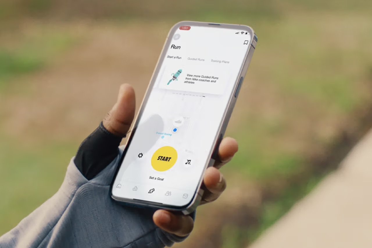 Person wearing a glove holding a smartphone with a running app open, showing a start button and map outdoors.