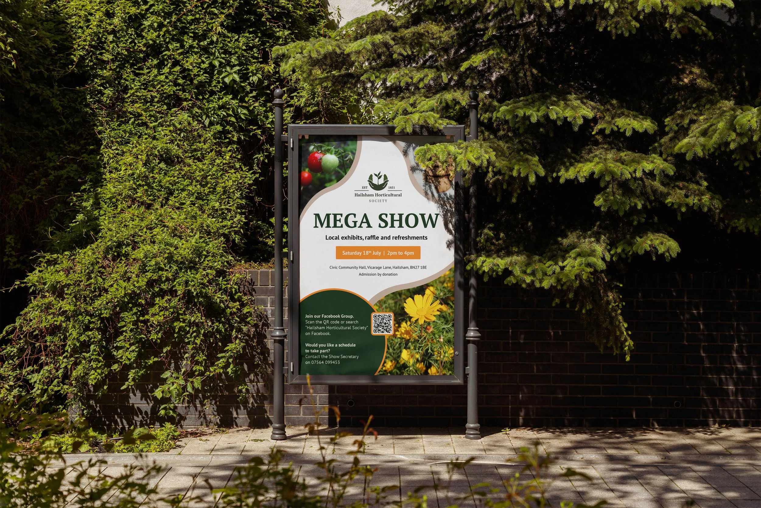 Sign advertising a horticultural society event with the text 'Mega Show', including details about date, time, location, and activities, surrounded by greenery and partially covered by tree branches.