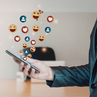 Person holding a smartphone with social media emojis and icons floating above it.
