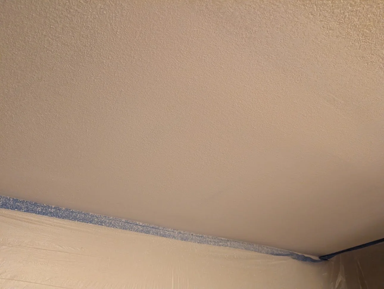 Upward view of a textured ceiling with painter's tape along the edges, where the ceiling meets the wall.