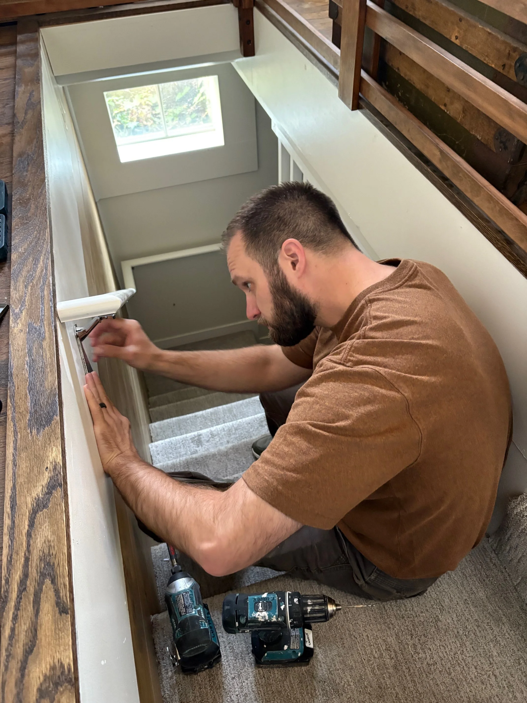 Man installing an interior handrail using a power drill, with tools on the floor.