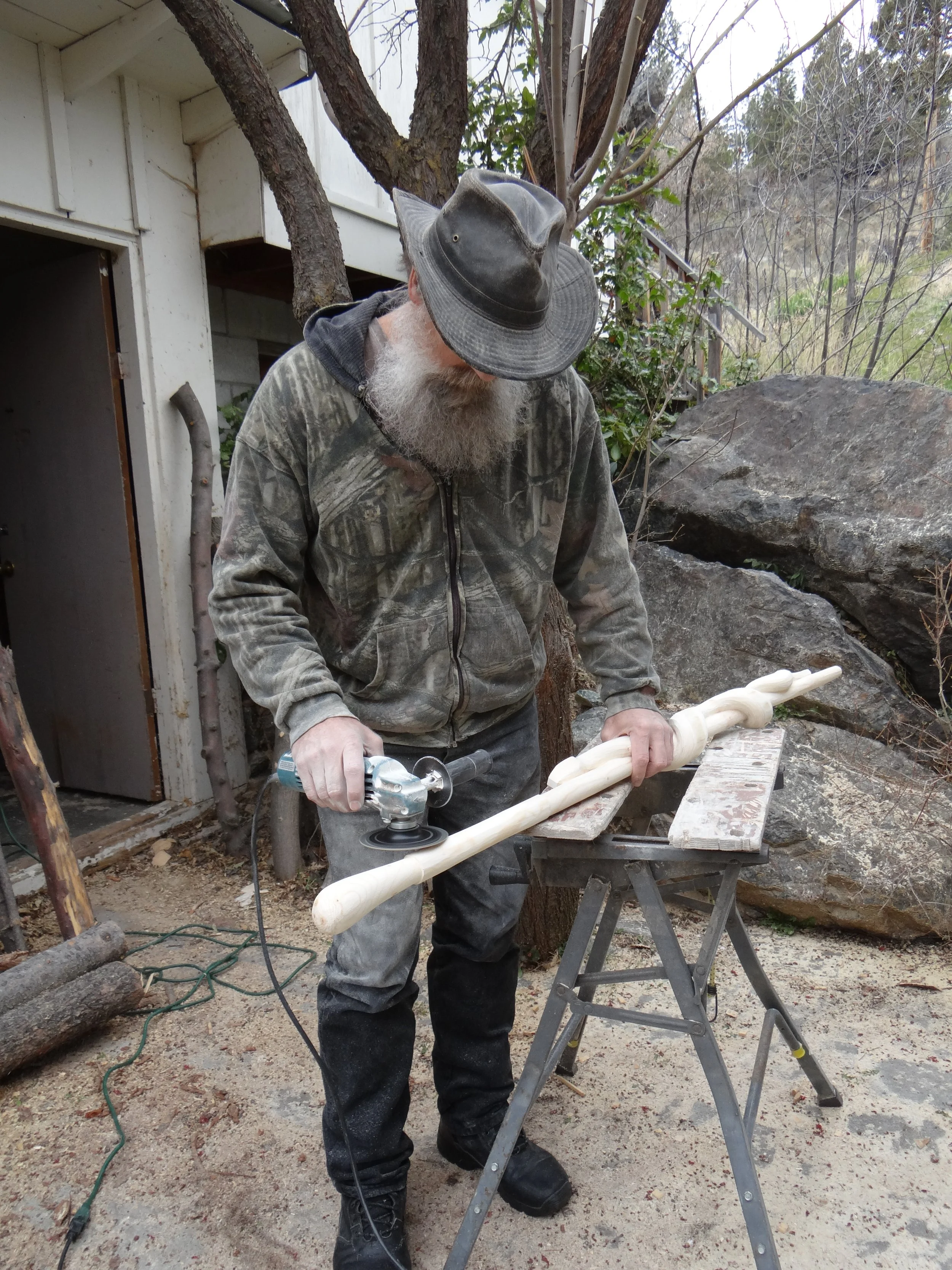 Mike Stinnett stands using a power carving tool to shape one of this rattlesnake walking sticks