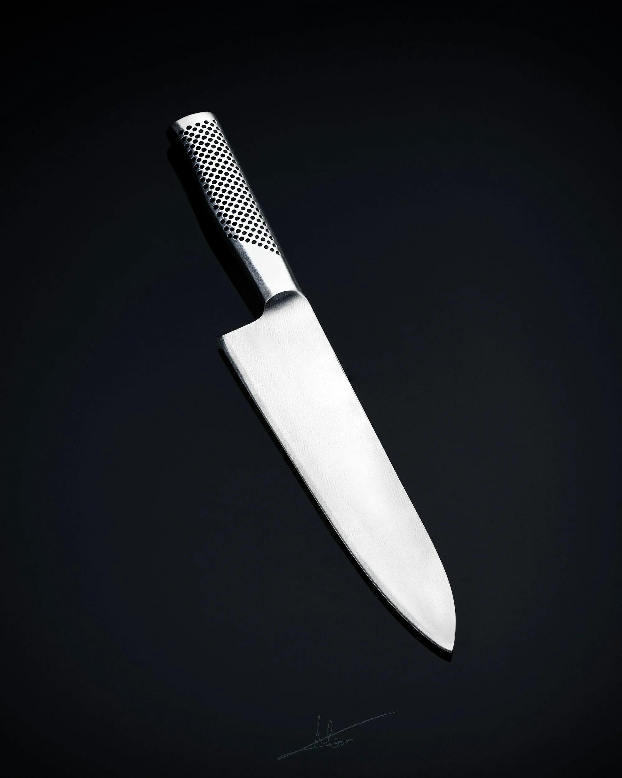Imagen de un cuchillo de chef plateado con mango perforado, sobre fondo negro.
