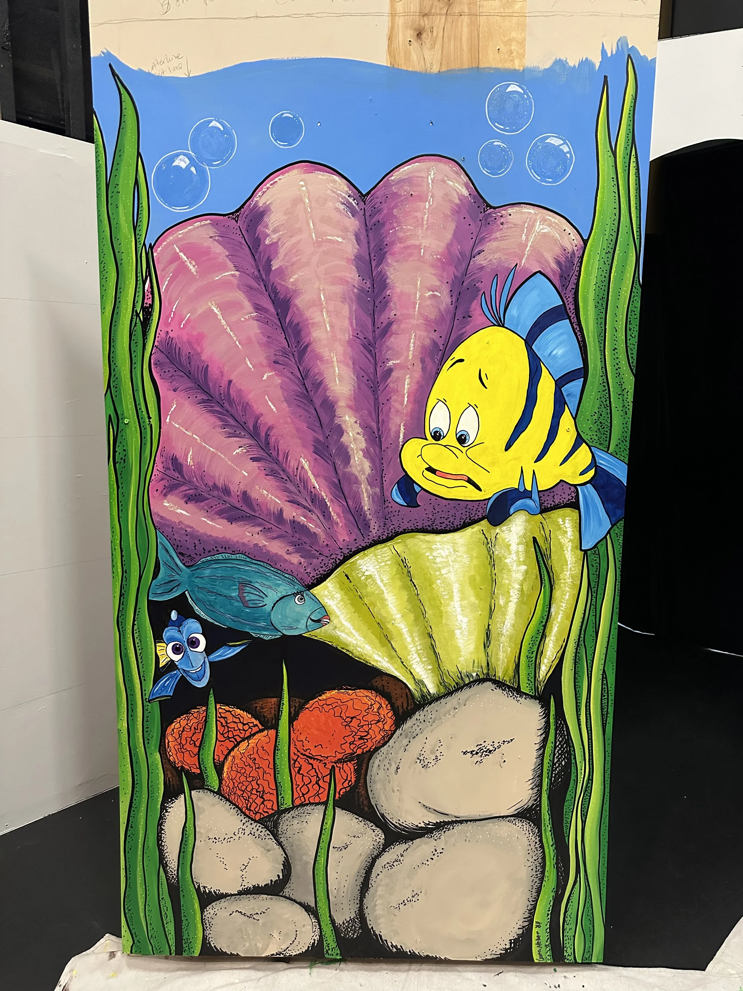 Colorful undersea scene featuring various fish, seaweeds, and seashells painted on a large wooden board.