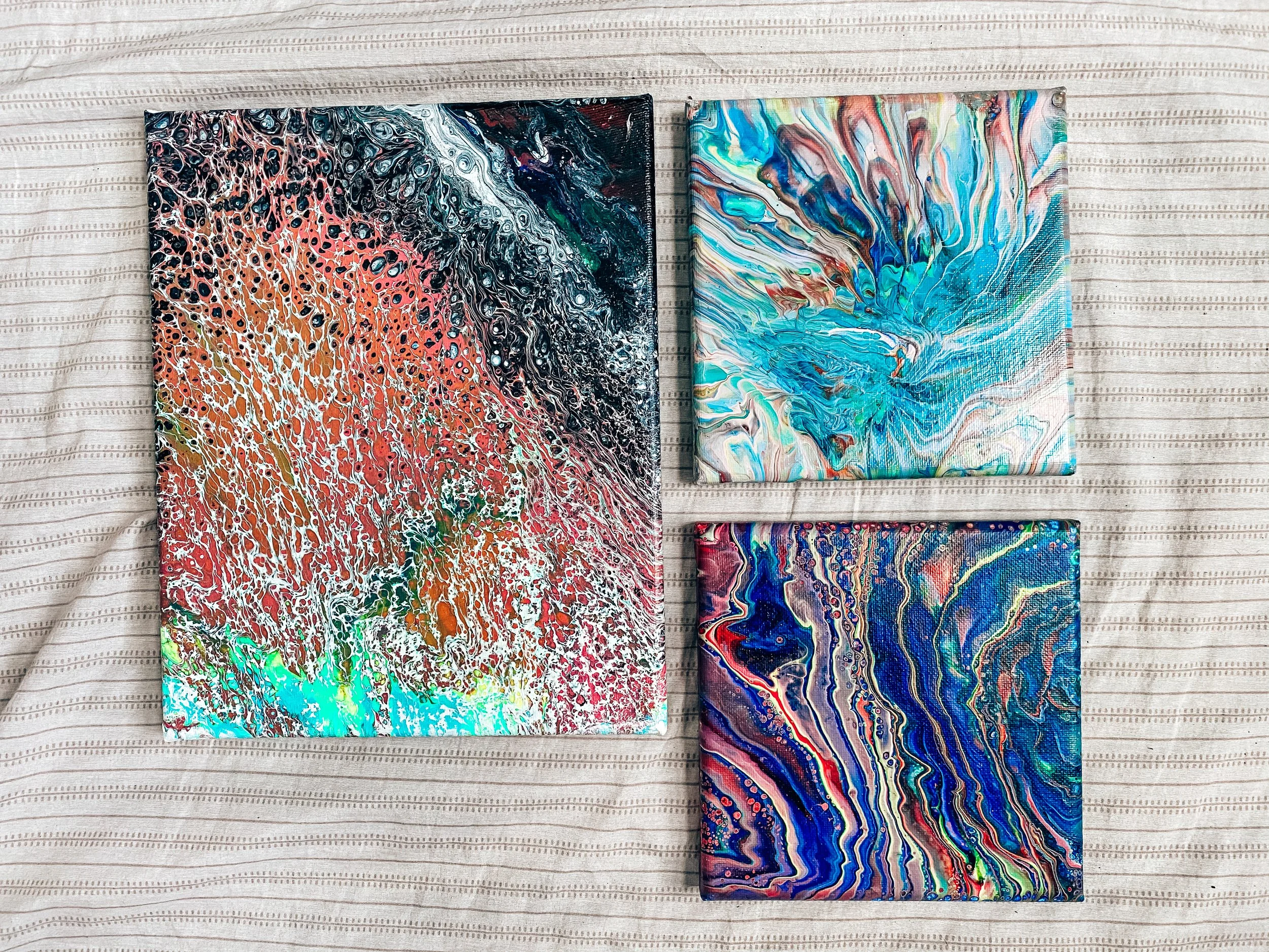 Four abstract paintings with colorful, swirling pattern on a light, striped fabric background.