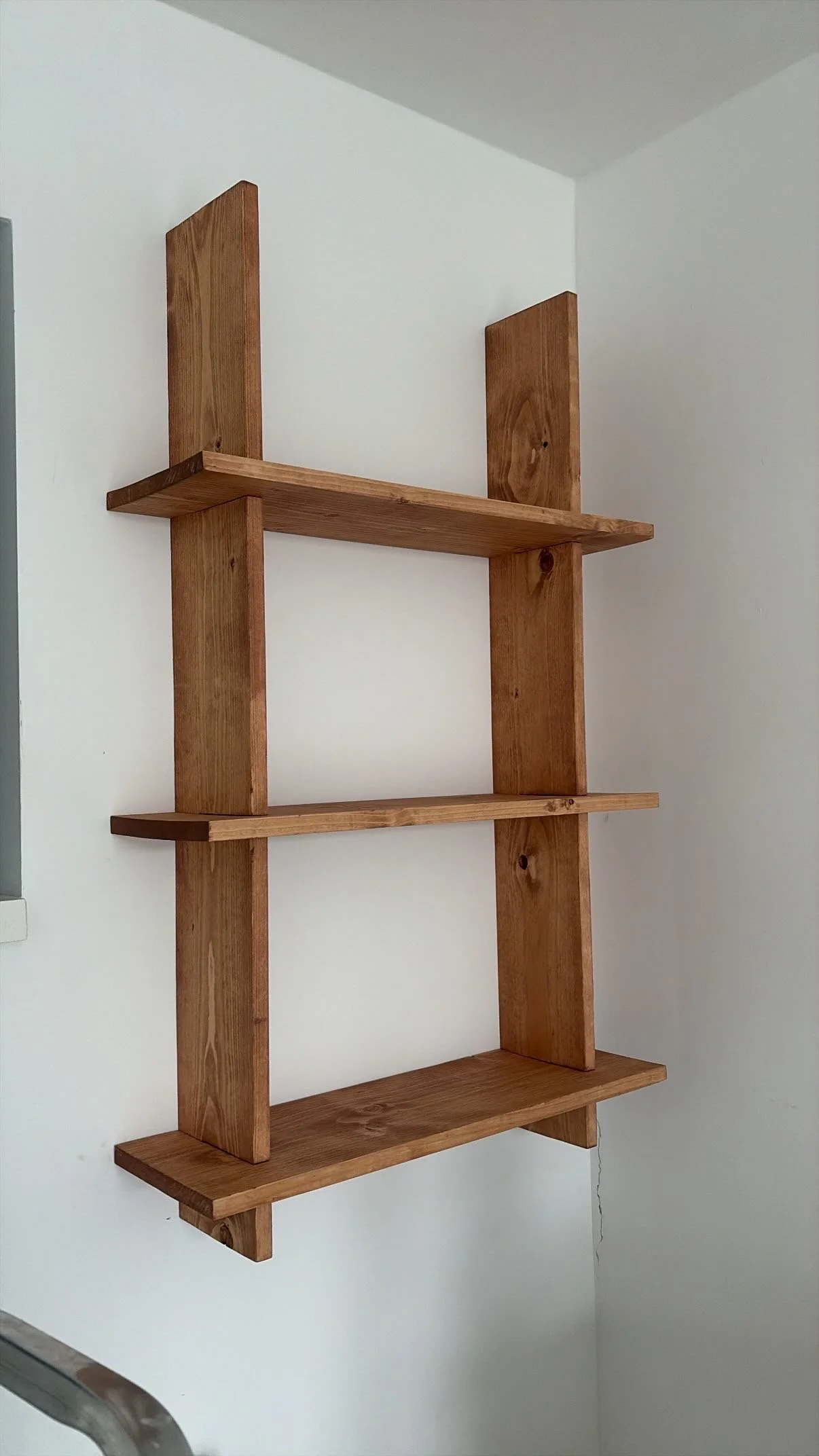Wooden wall-mounted shelf with multiple horizontal and vertical panels, installed on a white wall.