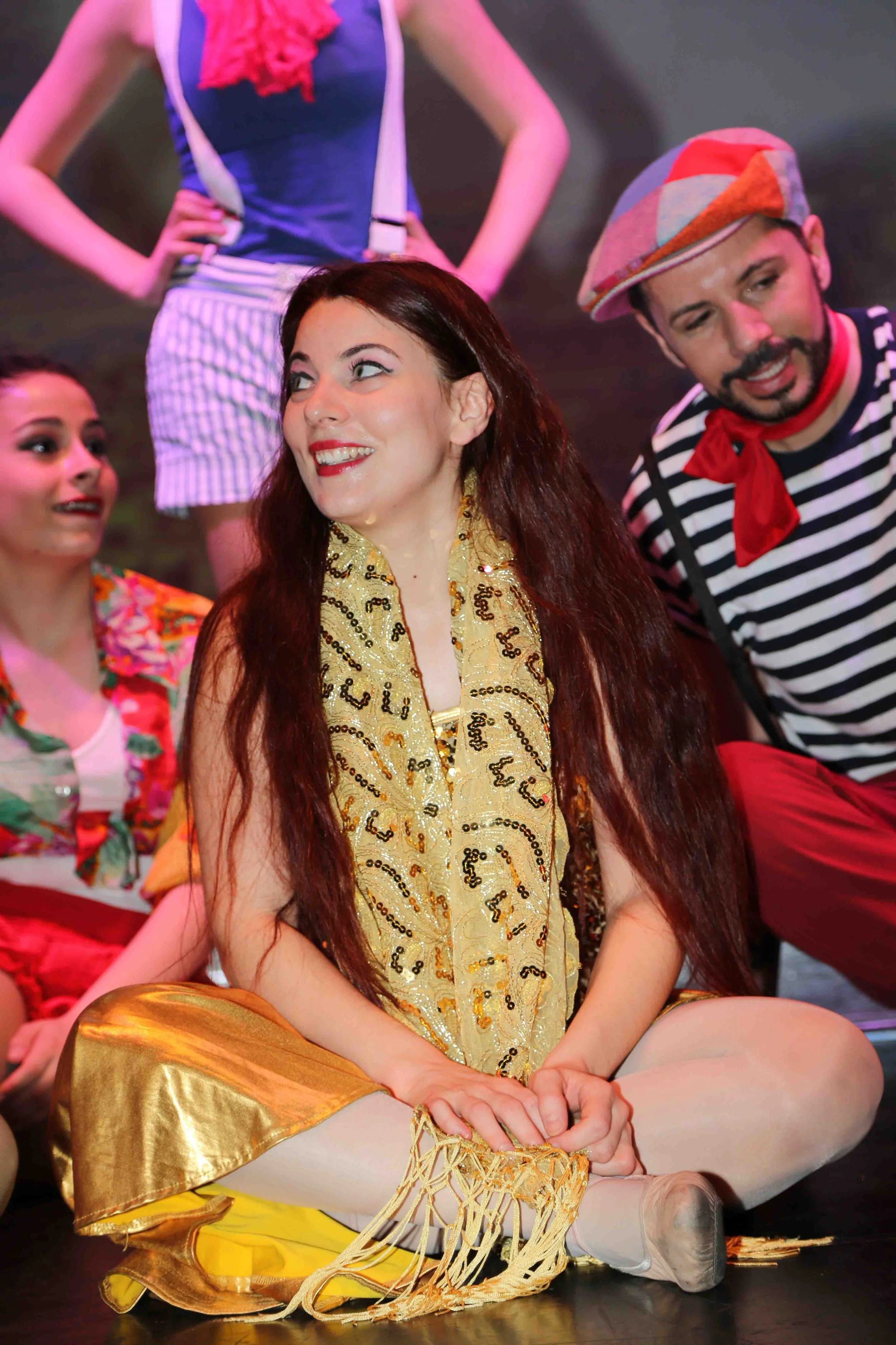 Un gruppo di ballerini in costumi colorati durante una performance teatrale, con uno sfondo scuro.