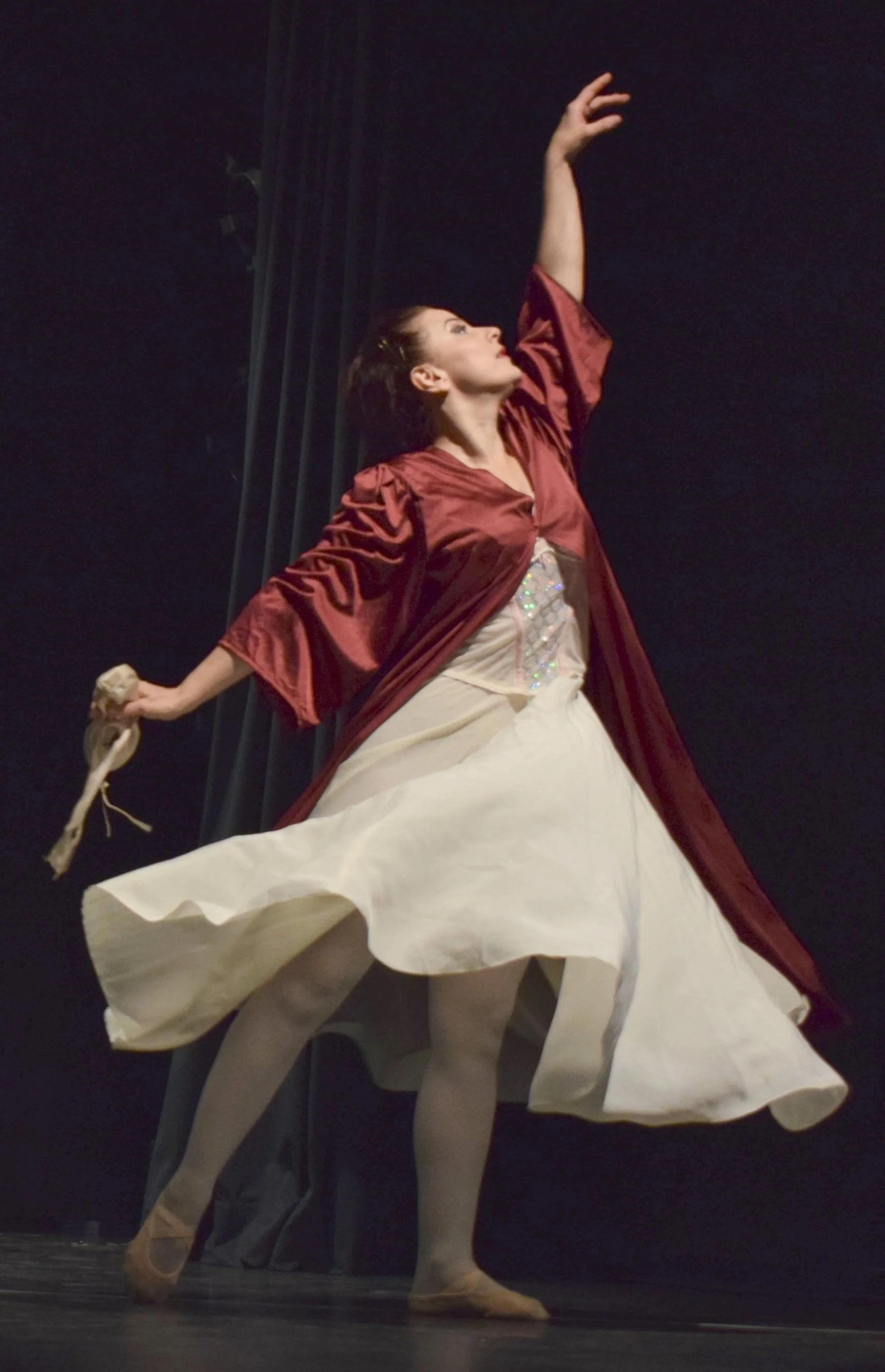 Ballerina in costume di scena con gonna bianca e mantello rosso, in una danza classica.