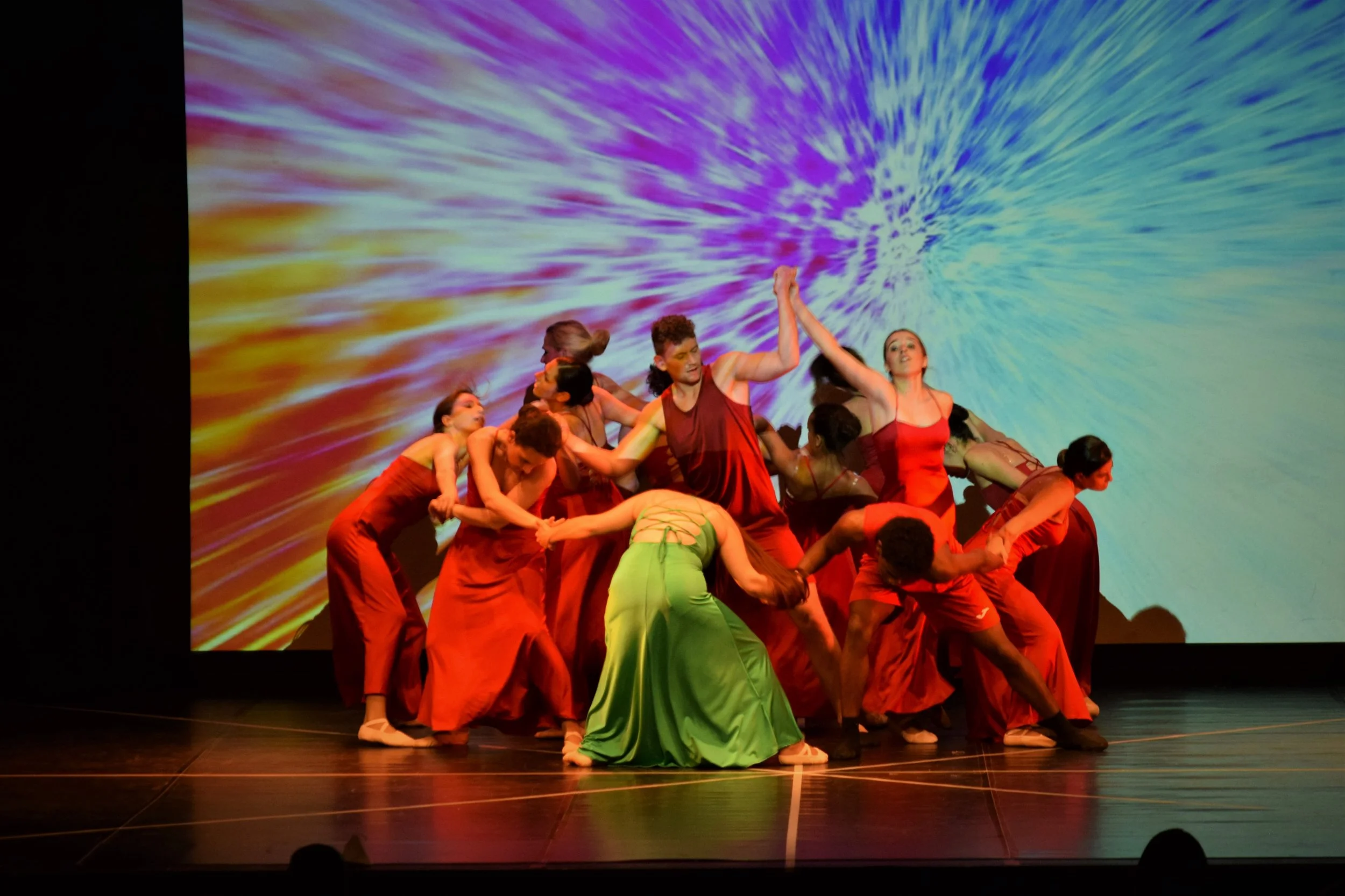 Gruppo di ballerini in costume colorato durante una performance sul palco con uno sfondo vibrante di luci e effetti visivi