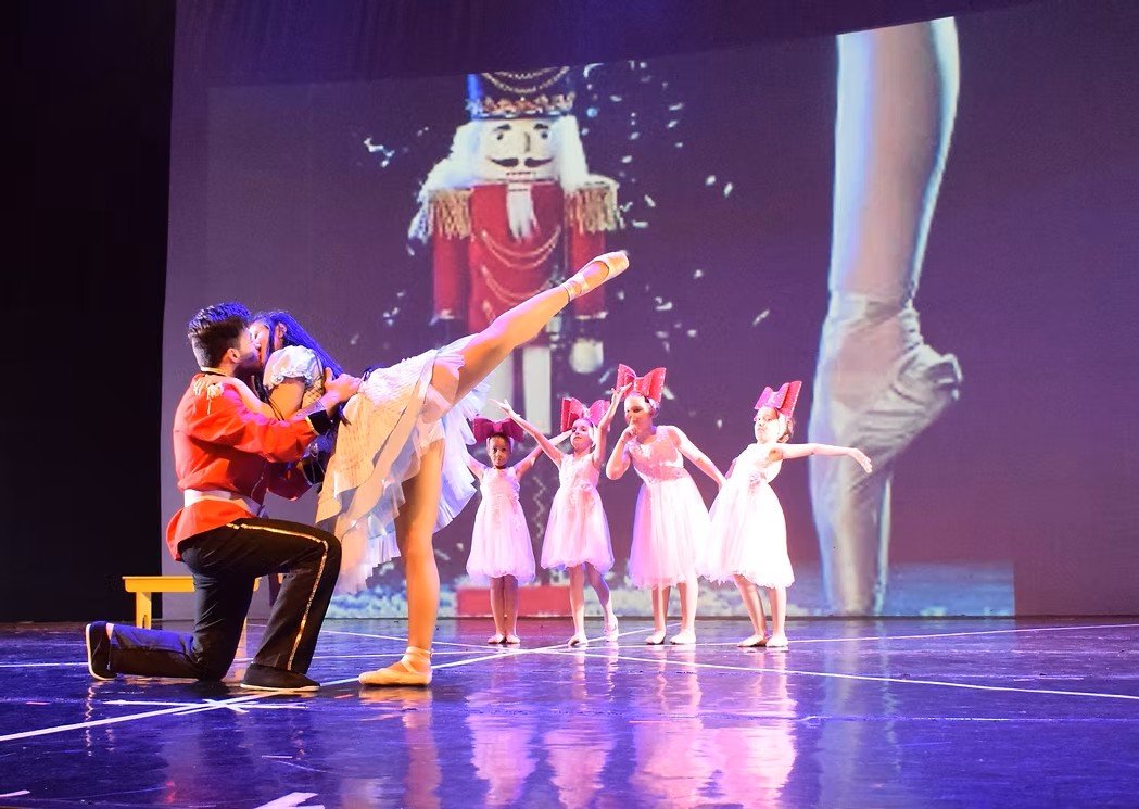 Bambini che ballano uno spettacolo di balletto su un palco, con un'immagine gigante di un burattino che si proietta sullo sfondo.