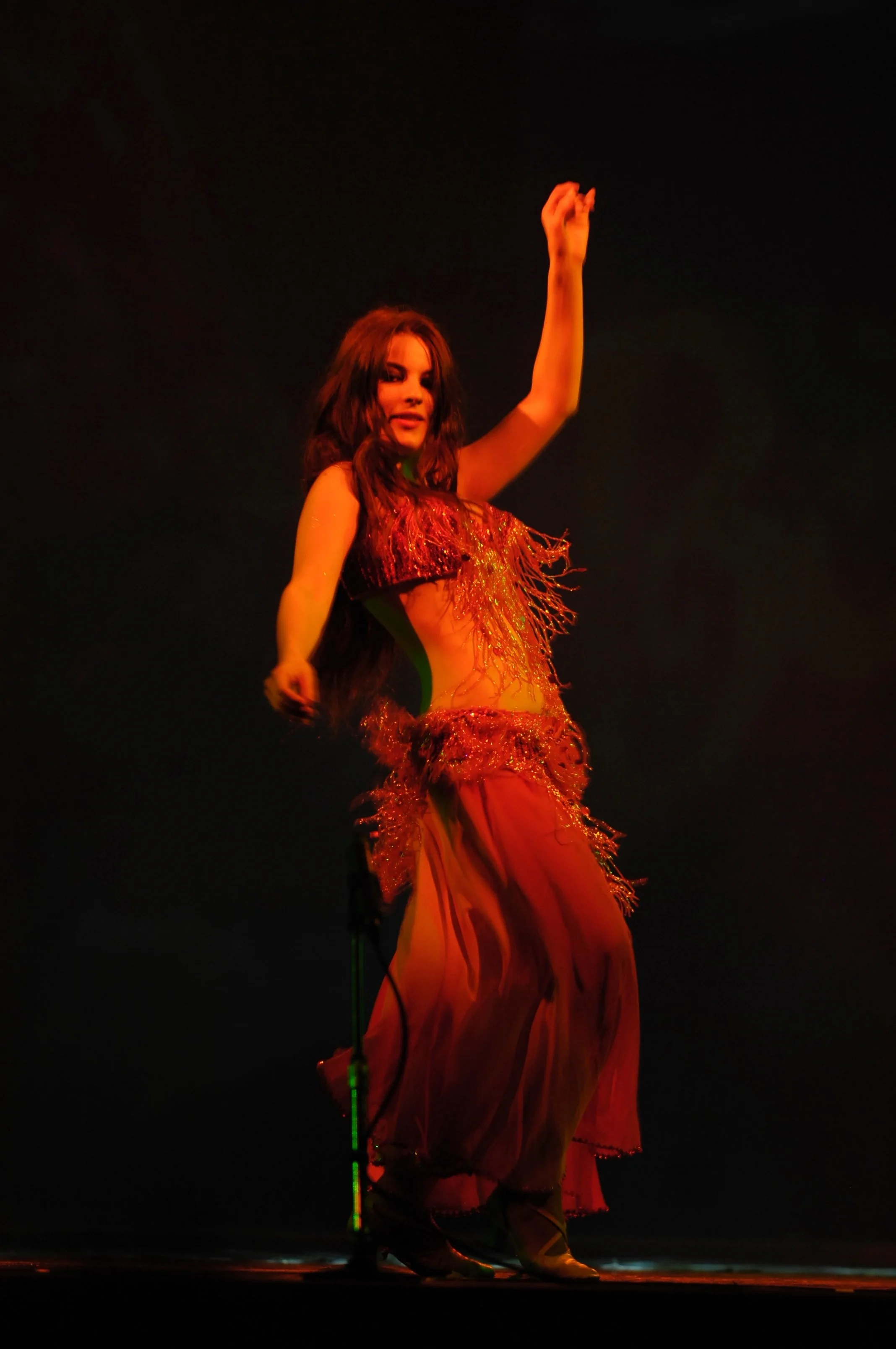 Donna che danza in costume da danza orientale fucsia con dettagli dorati sotto luci calde.