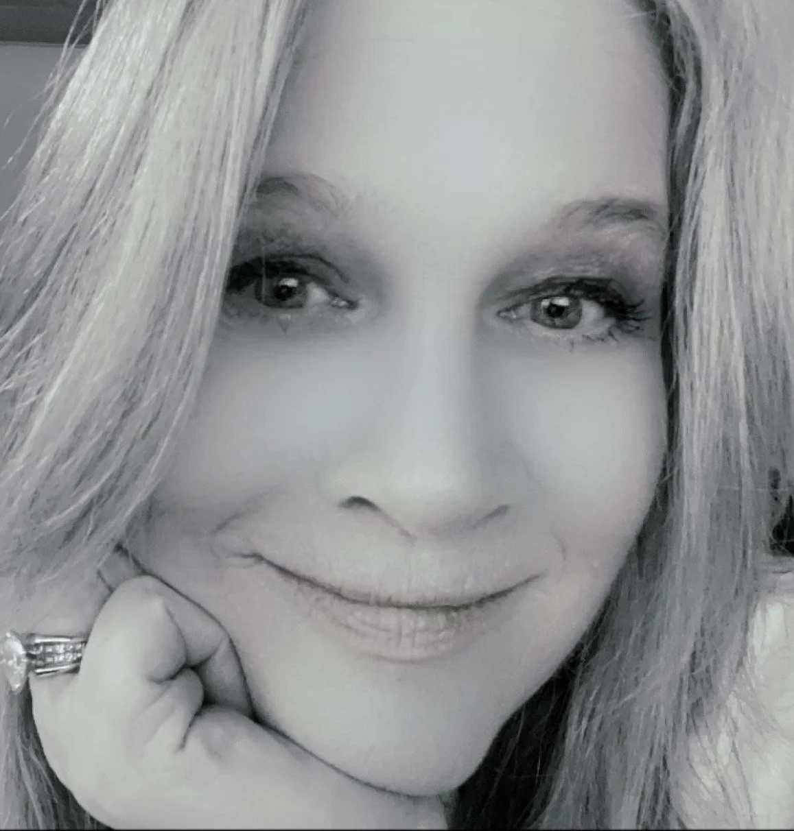 A black-and-white close-up of a woman smiling softly, resting her chin on her hand.