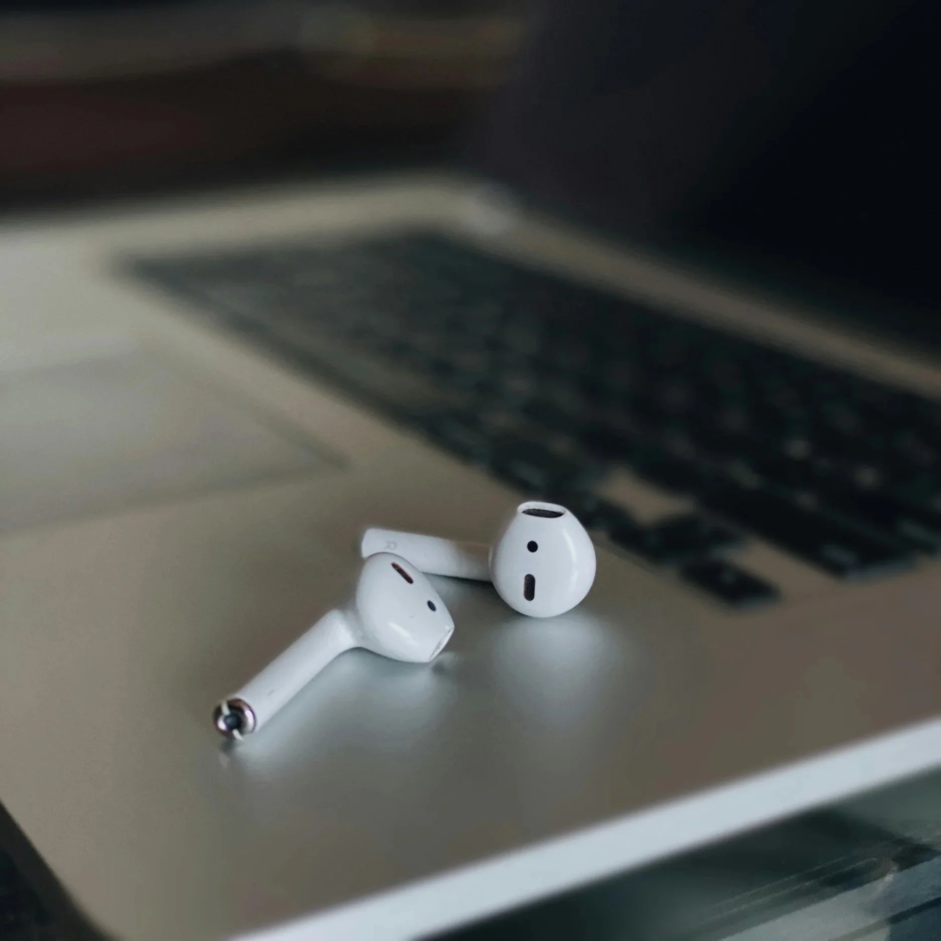 Close-up photo of a pair of white wireless earbuds on a gray surface.