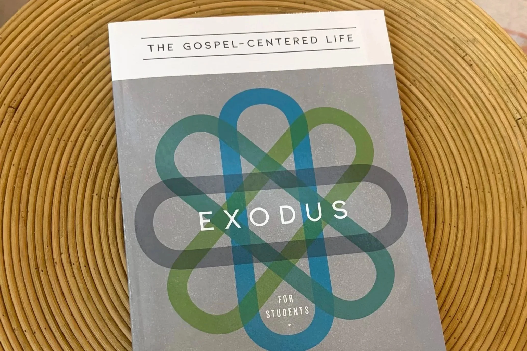 A booklet titled "The Gospel-Centered Life" with a colorful overlapping heart design on the cover, resting on a circular wicker placemat.