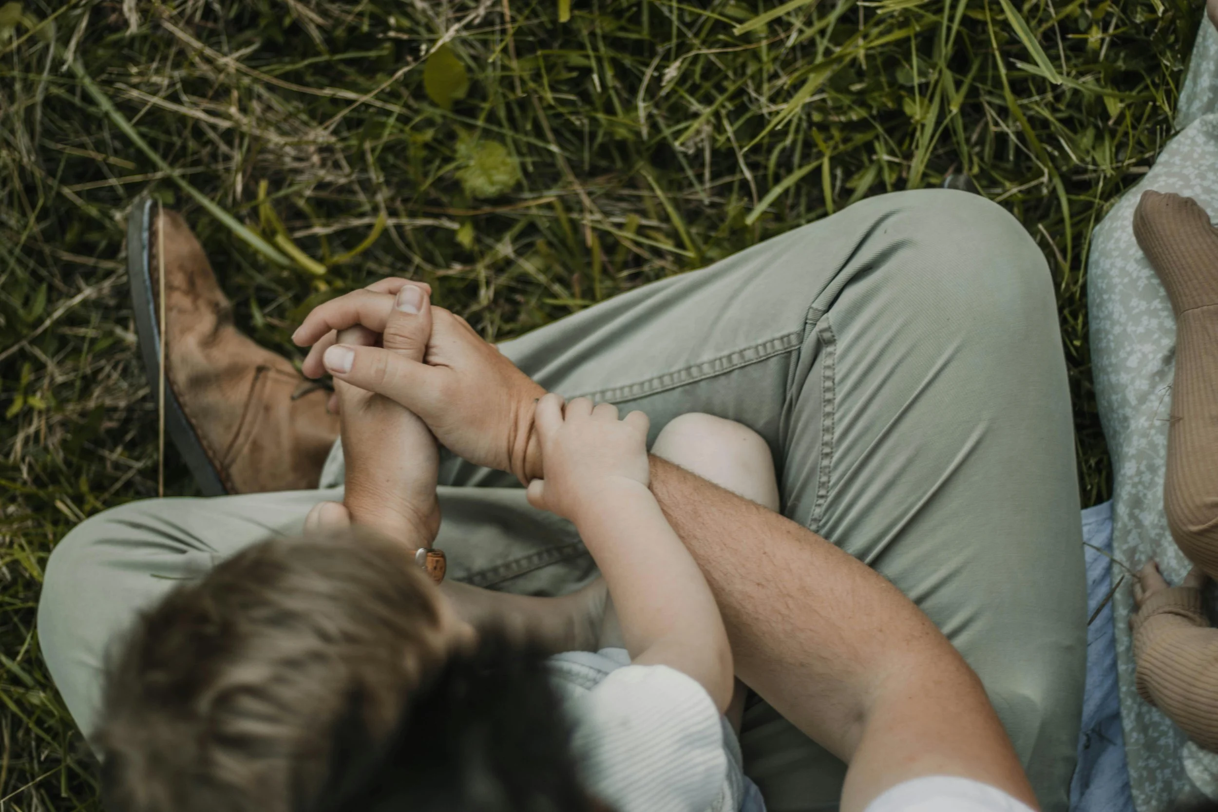 A person and child sitting on grass, holding hands.