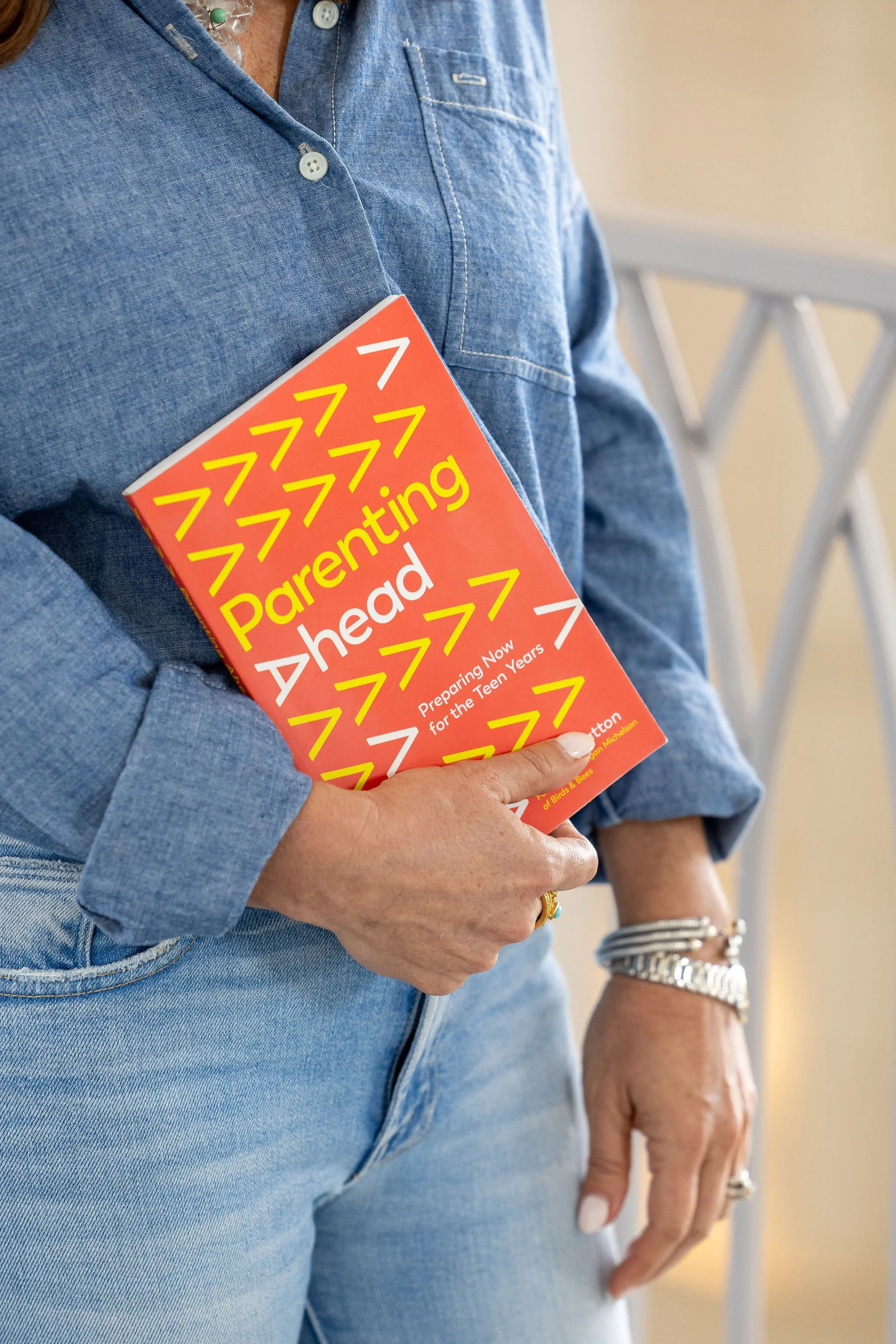 A person wearing a blue denim shirt holding a book titled 'Parenting Ahead: Preparing Now for the Teen Years' against a beige wall.